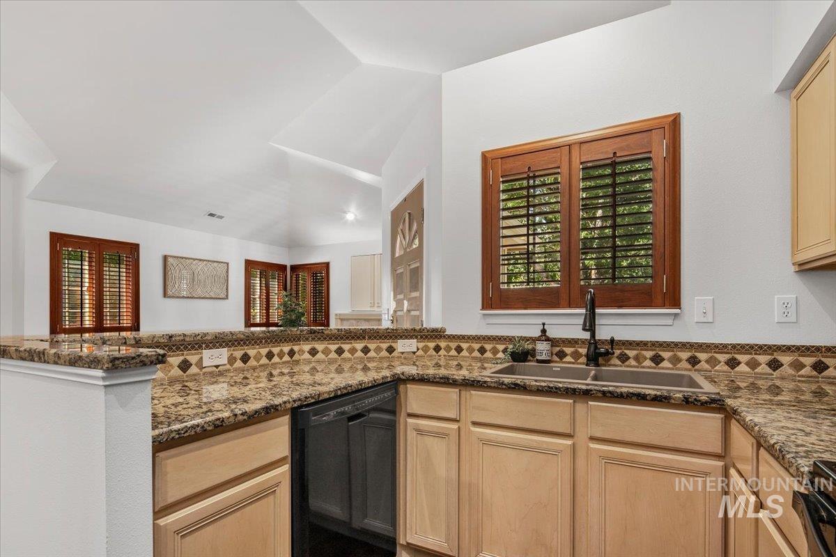 Kitchen with light brown cabinetry, dishwasher, and granite countertops