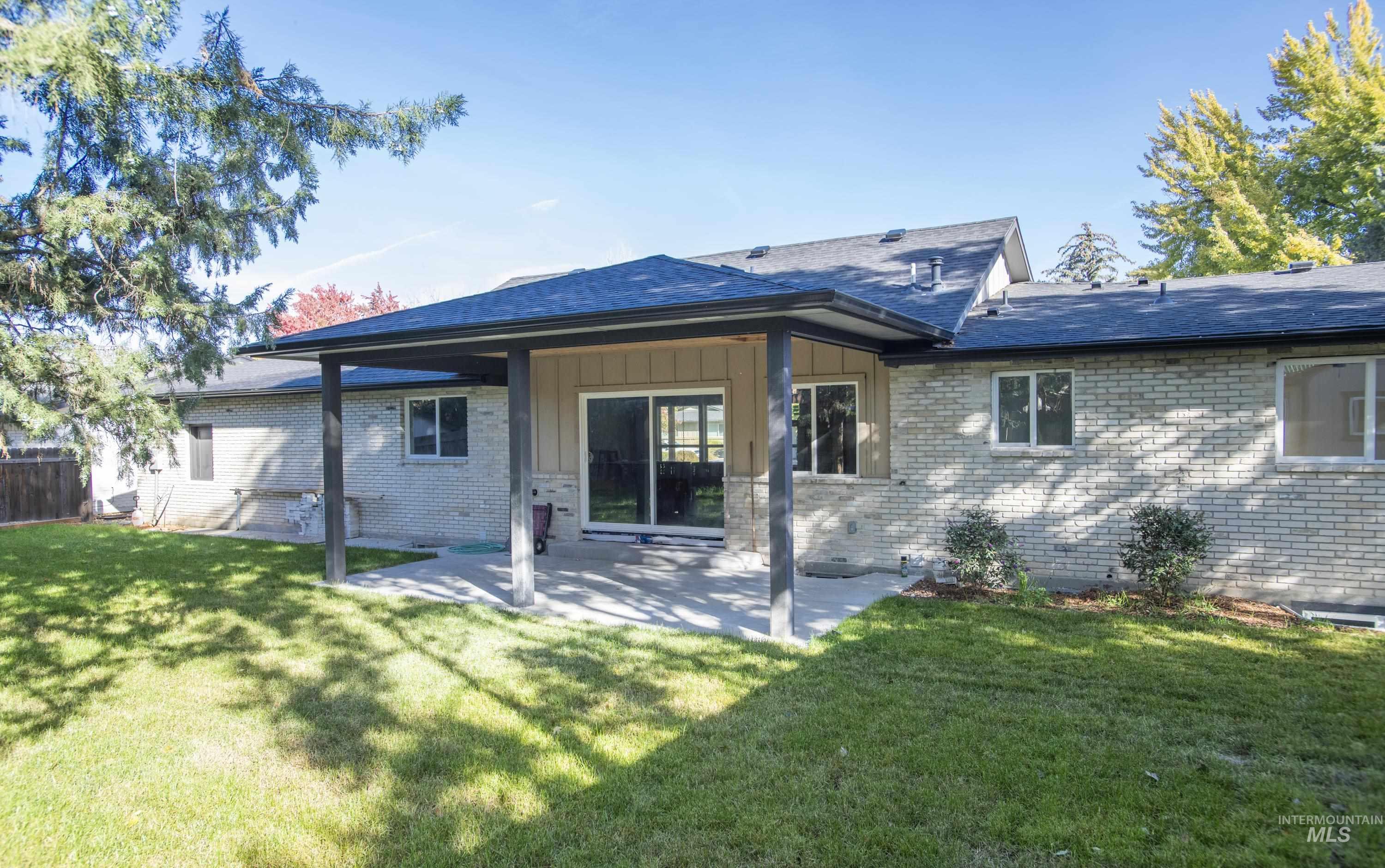 Back of house featuring a patio area, brick siding, board and batten siding, and a shingled roof