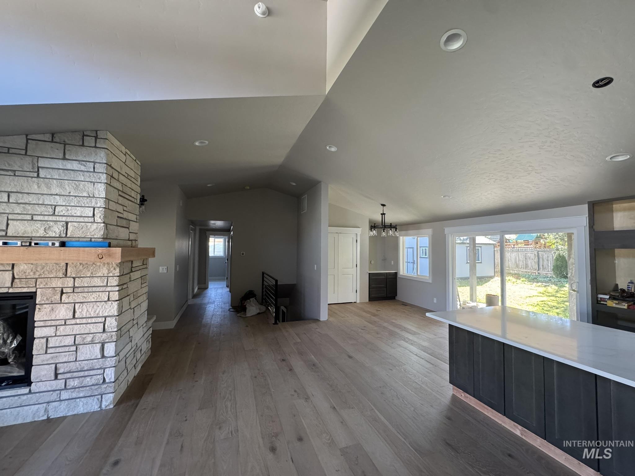 Unfurnished living room featuring light wood finished floors, lofted ceiling, healthy amount of natural light, a chandelier, and a fireplace