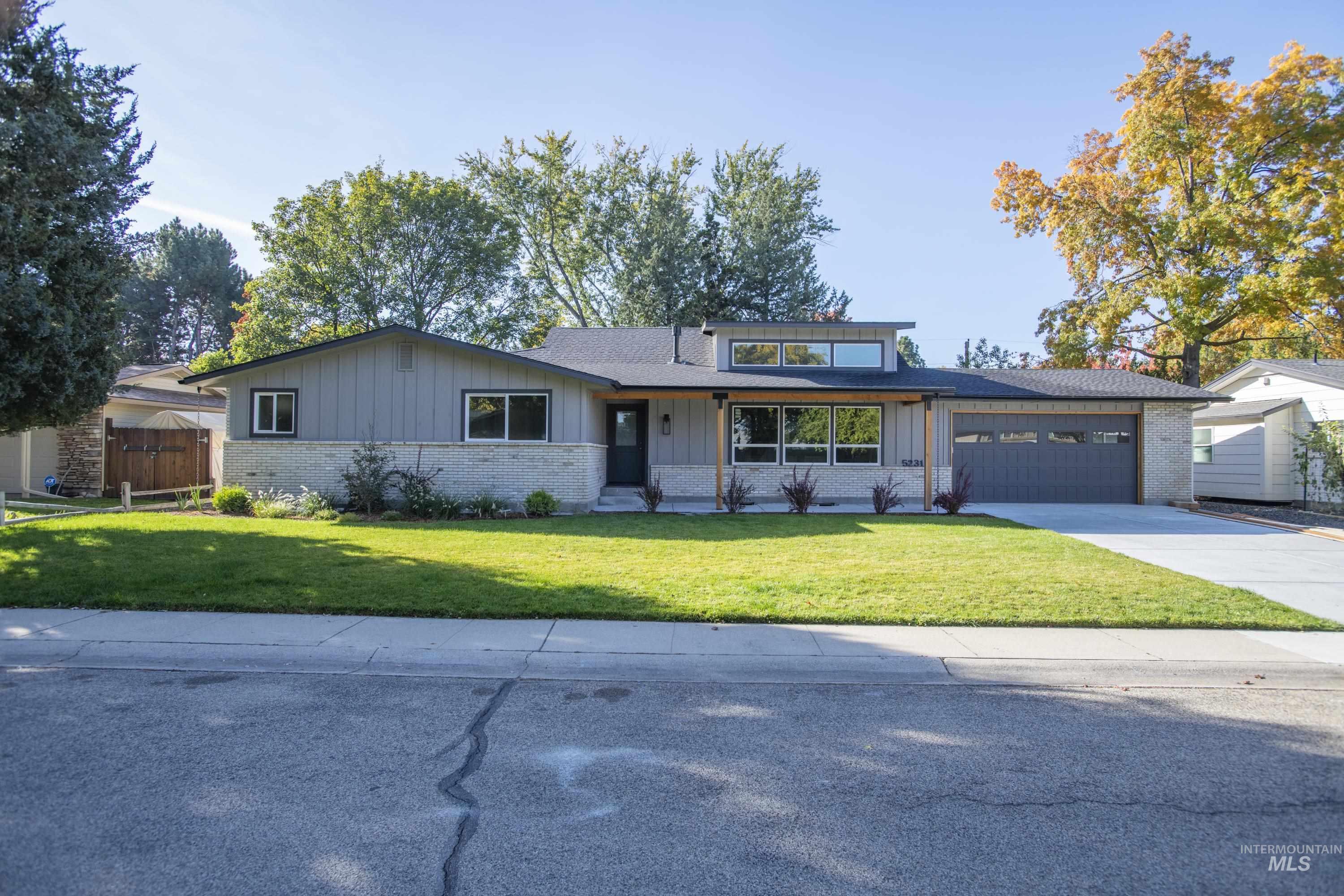 View of front of house with brick siding, board and batten siding, a front lawn, driveway, and an attached garage