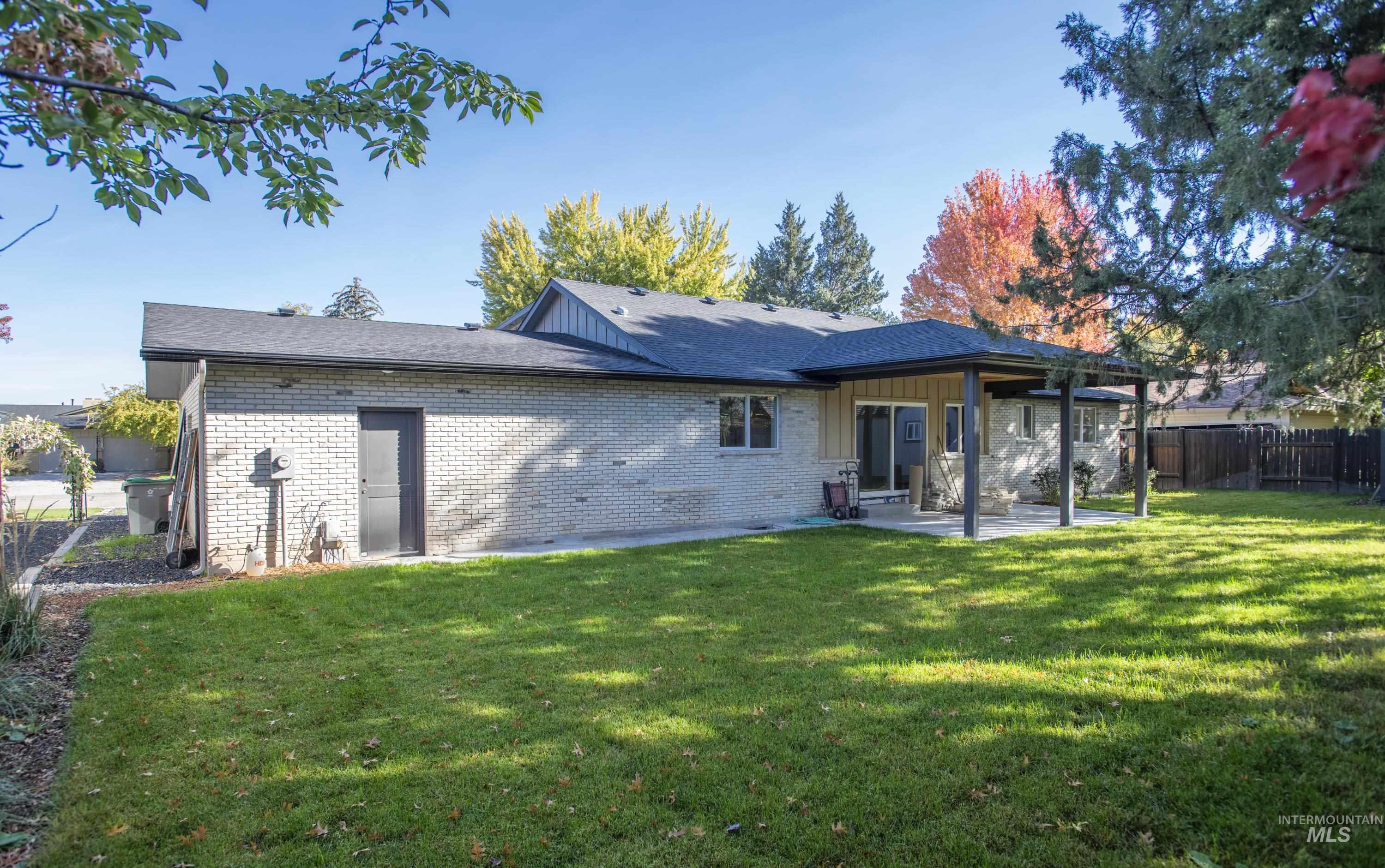 Rear view of house with brick siding, a patio area, board and batten siding, and a shingled roof