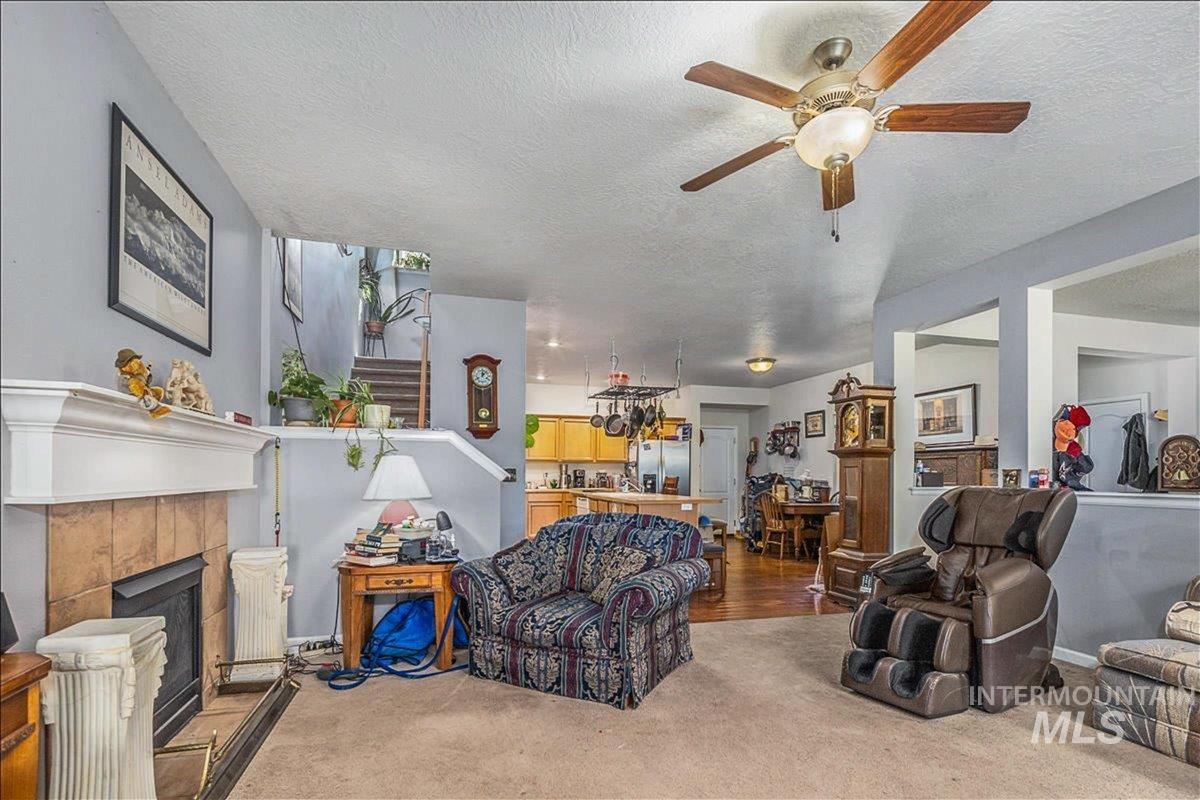 Living room featuring a tile fireplace, ceiling fan, wood finished floors, a textured ceiling, and stairway