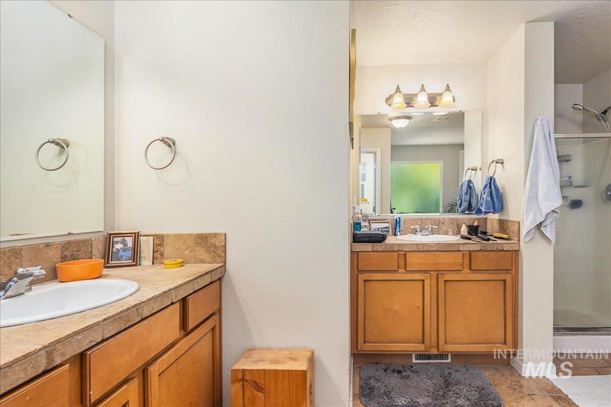 Bathroom featuring a stall shower, two vanities, a textured ceiling, and light tile patterned floors