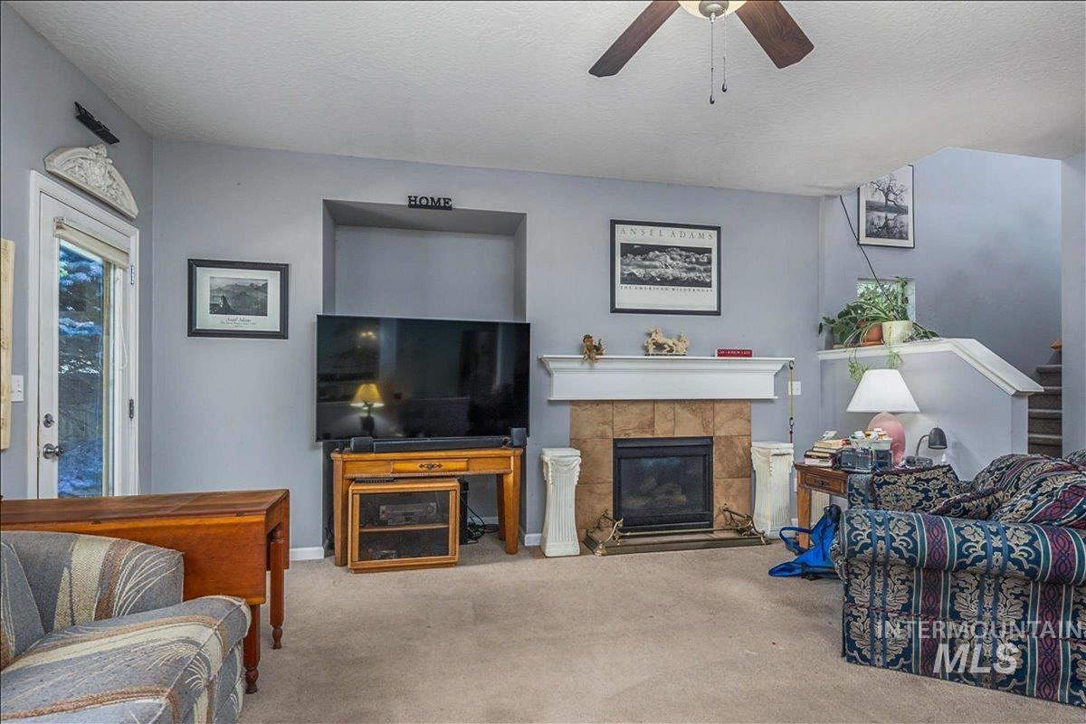 Carpeted living area featuring a tile fireplace, a textured ceiling, ceiling fan, and stairway