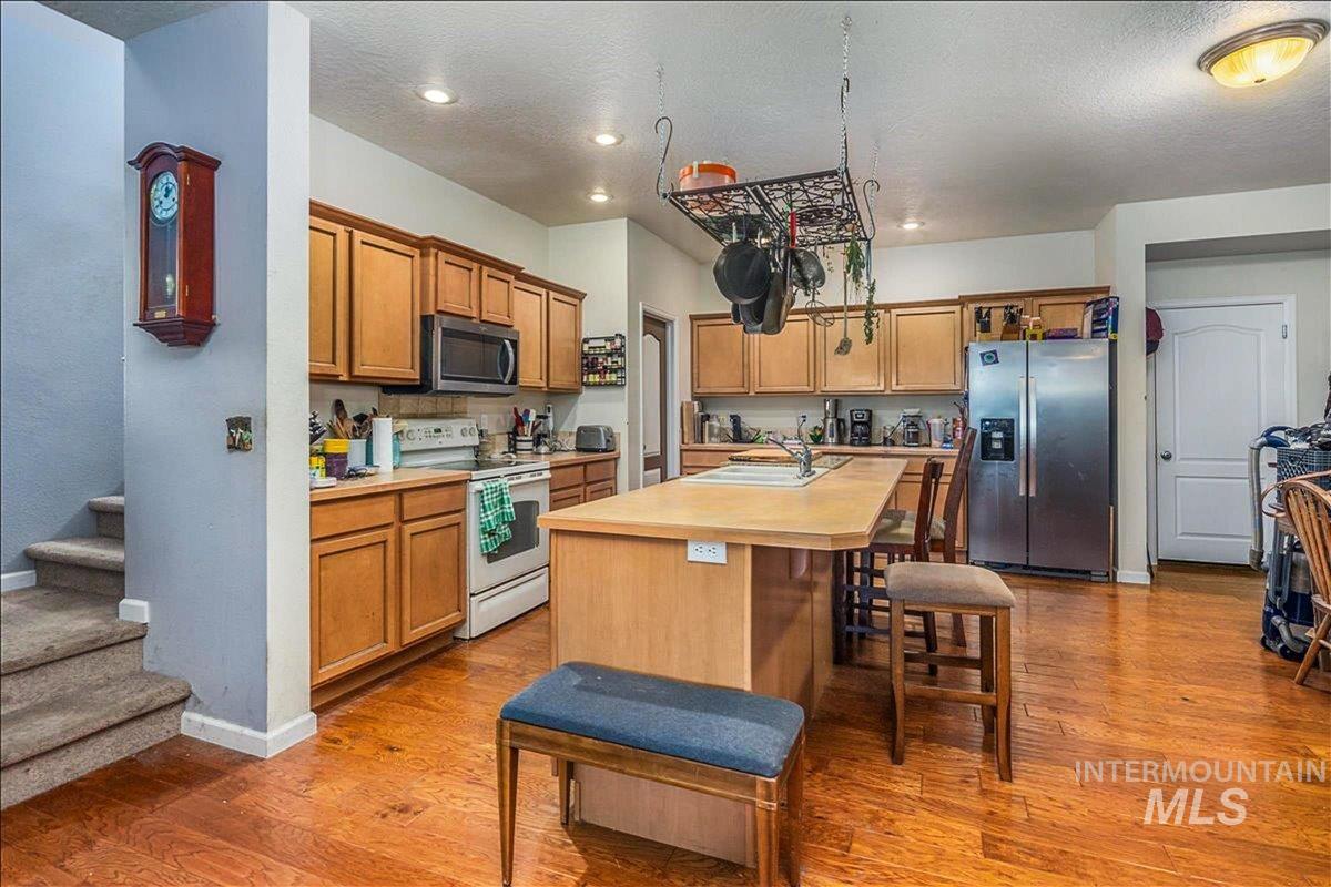 Kitchen featuring light countertops, stainless steel appliances, an island with sink, light wood finished floors, and a kitchen bar