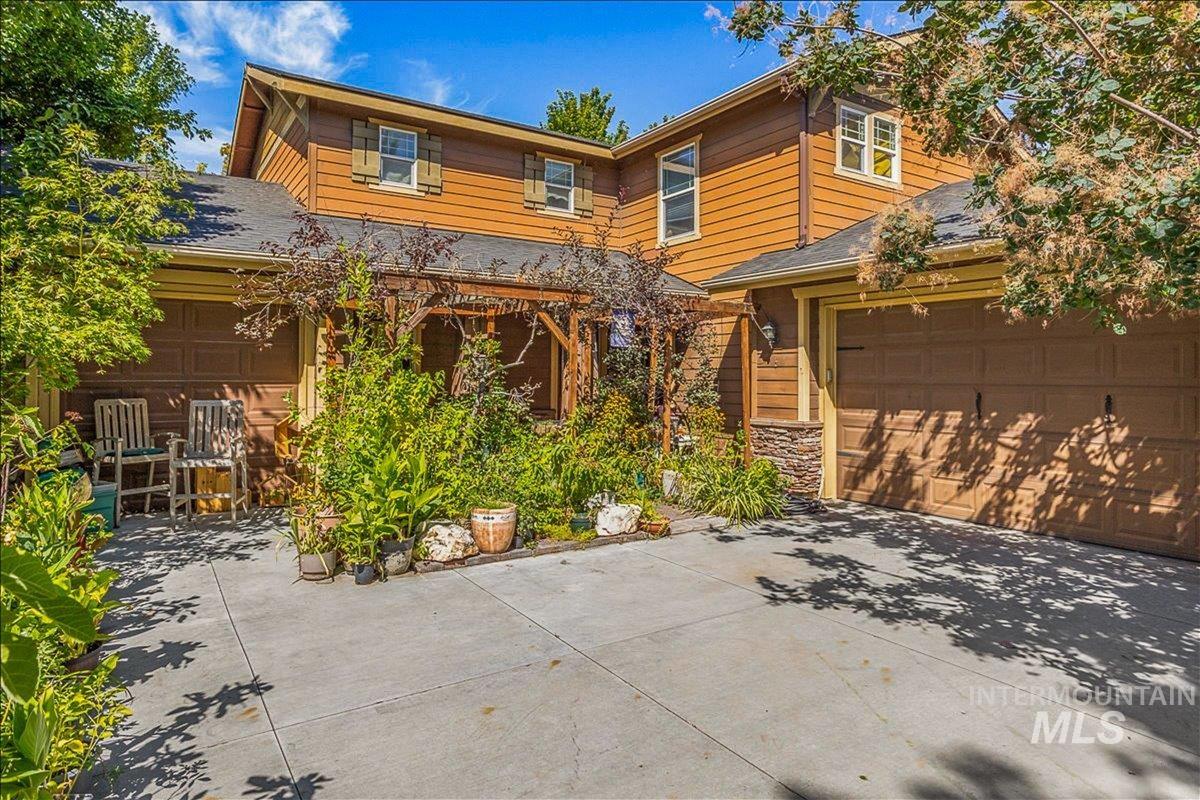View of front of home featuring driveway, a garage, a patio, stone siding, and a shingled roof