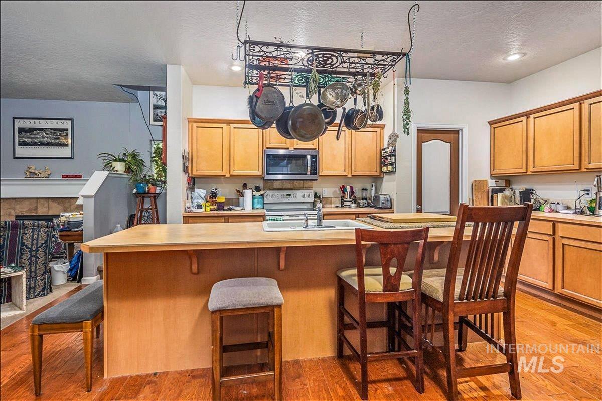 Kitchen featuring a breakfast bar, light countertops, light wood-style flooring, stainless steel appliances, and a center island with sink