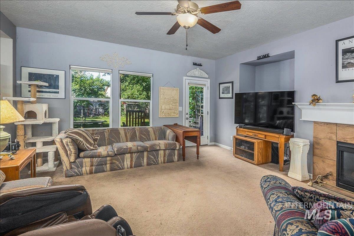 Carpeted living area featuring a textured ceiling, a tiled fireplace, and a ceiling fan