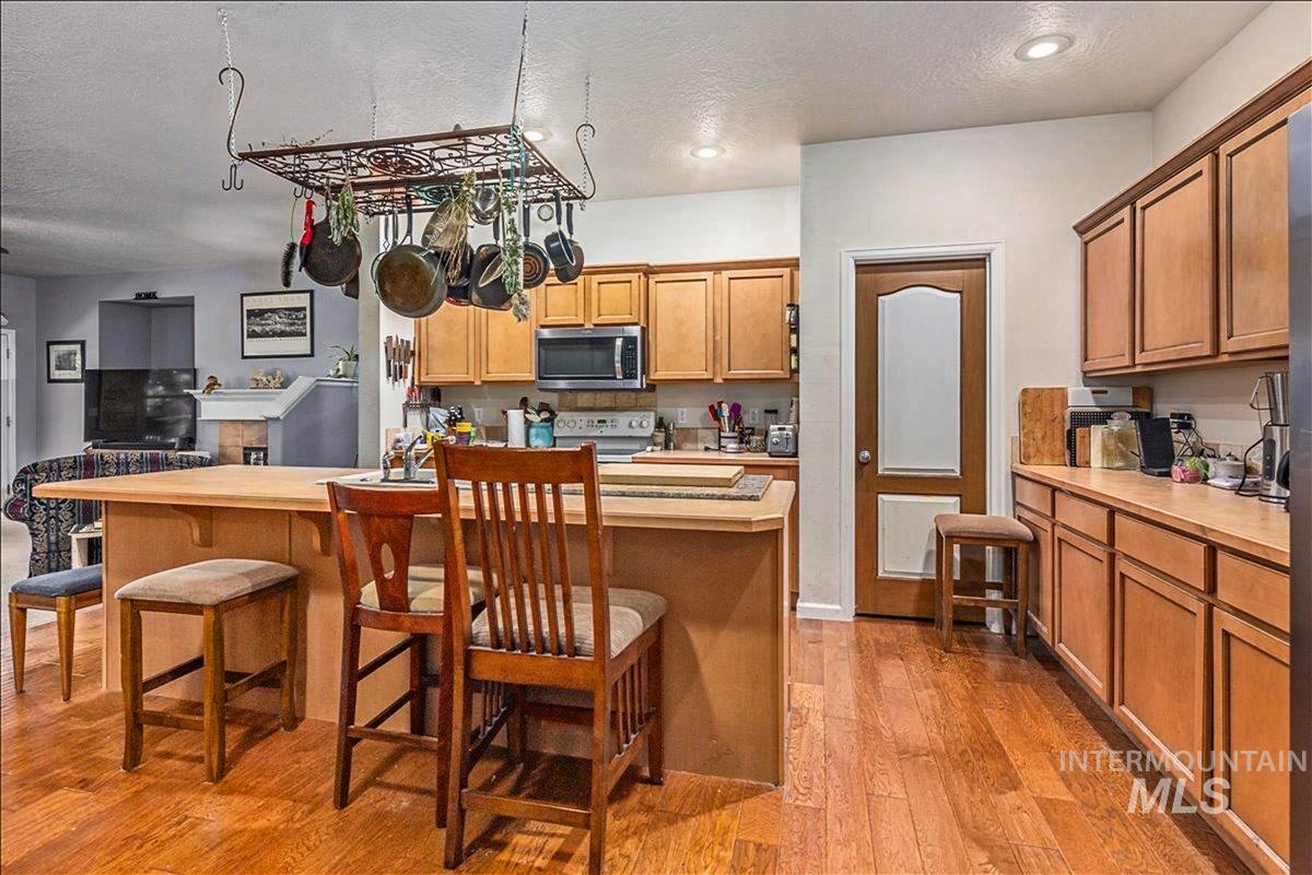 Kitchen with a breakfast bar area, brown cabinetry, light countertops, stainless steel microwave, and a textured ceiling