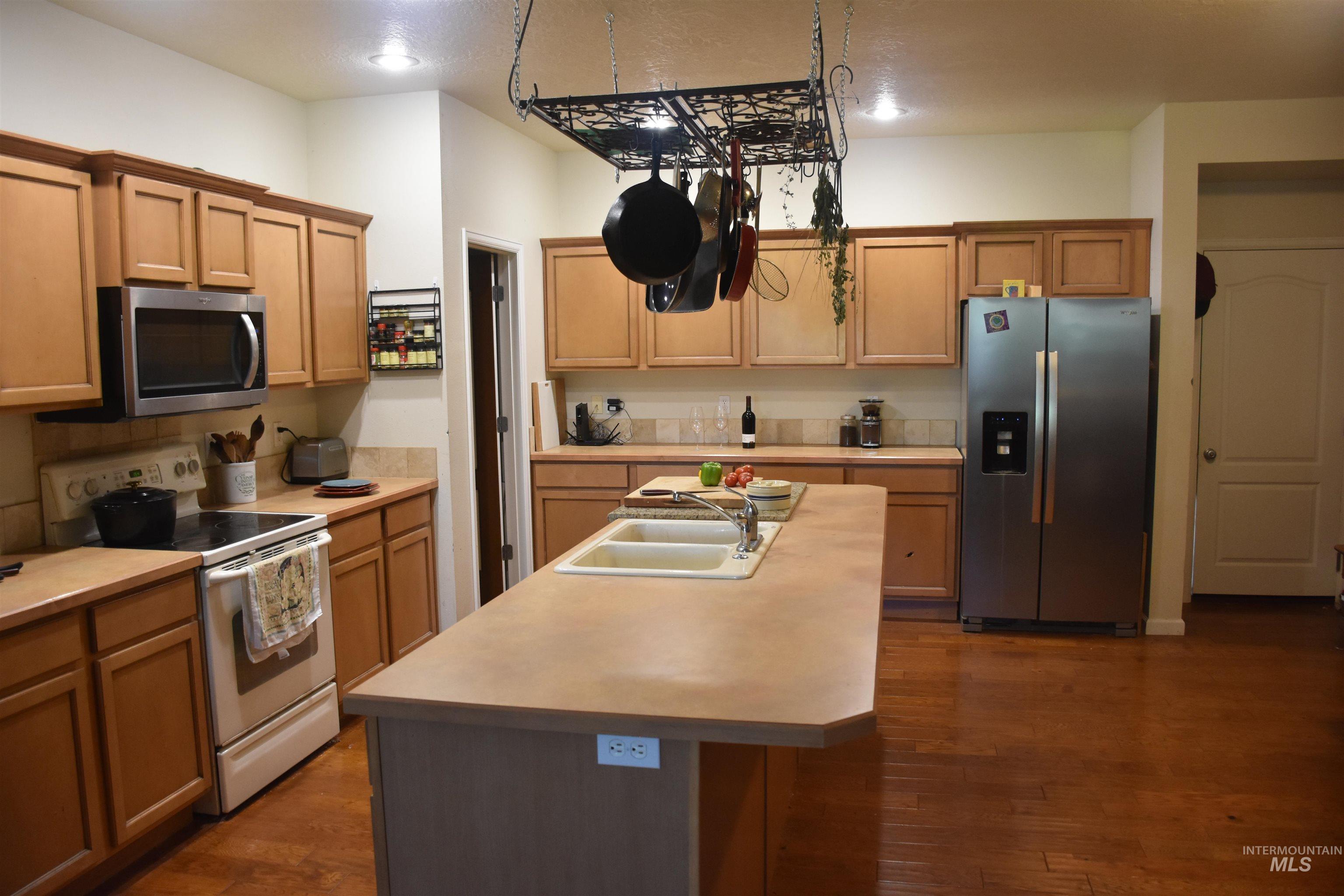 Kitchen with stainless steel appliances, a kitchen island with sink, light countertops, and dark wood-style floors