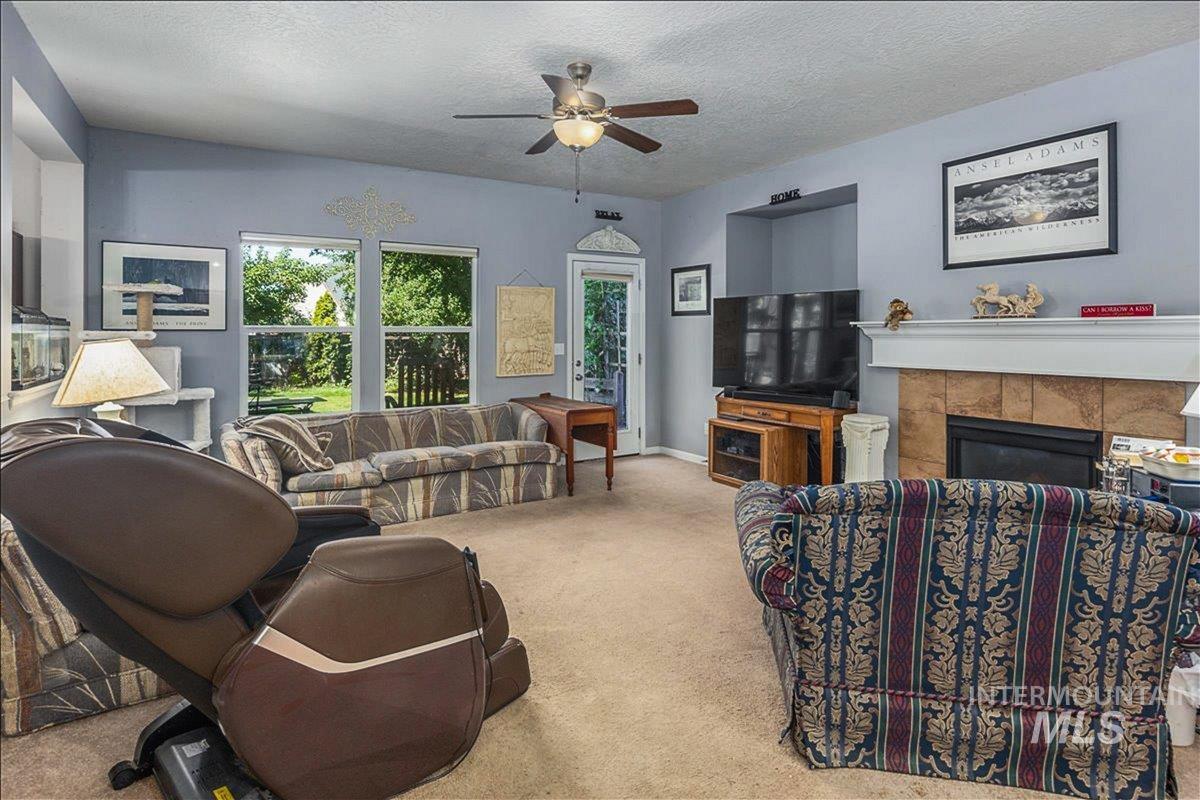 Living room with carpet flooring, a textured ceiling, a fireplace, and a ceiling fan