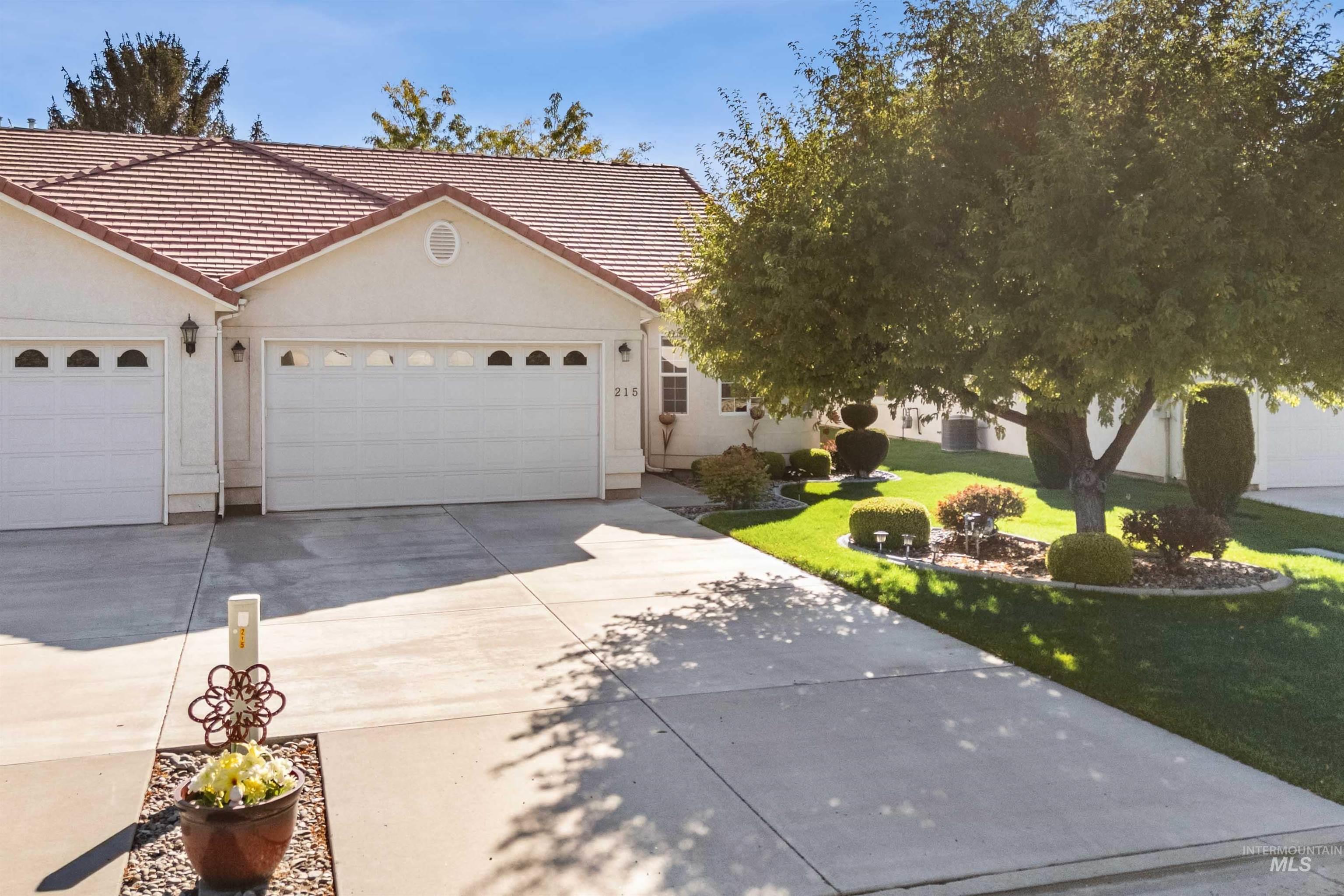 Ranch-style house with a tile roof, driveway, a front lawn, an attached garage, and stucco siding