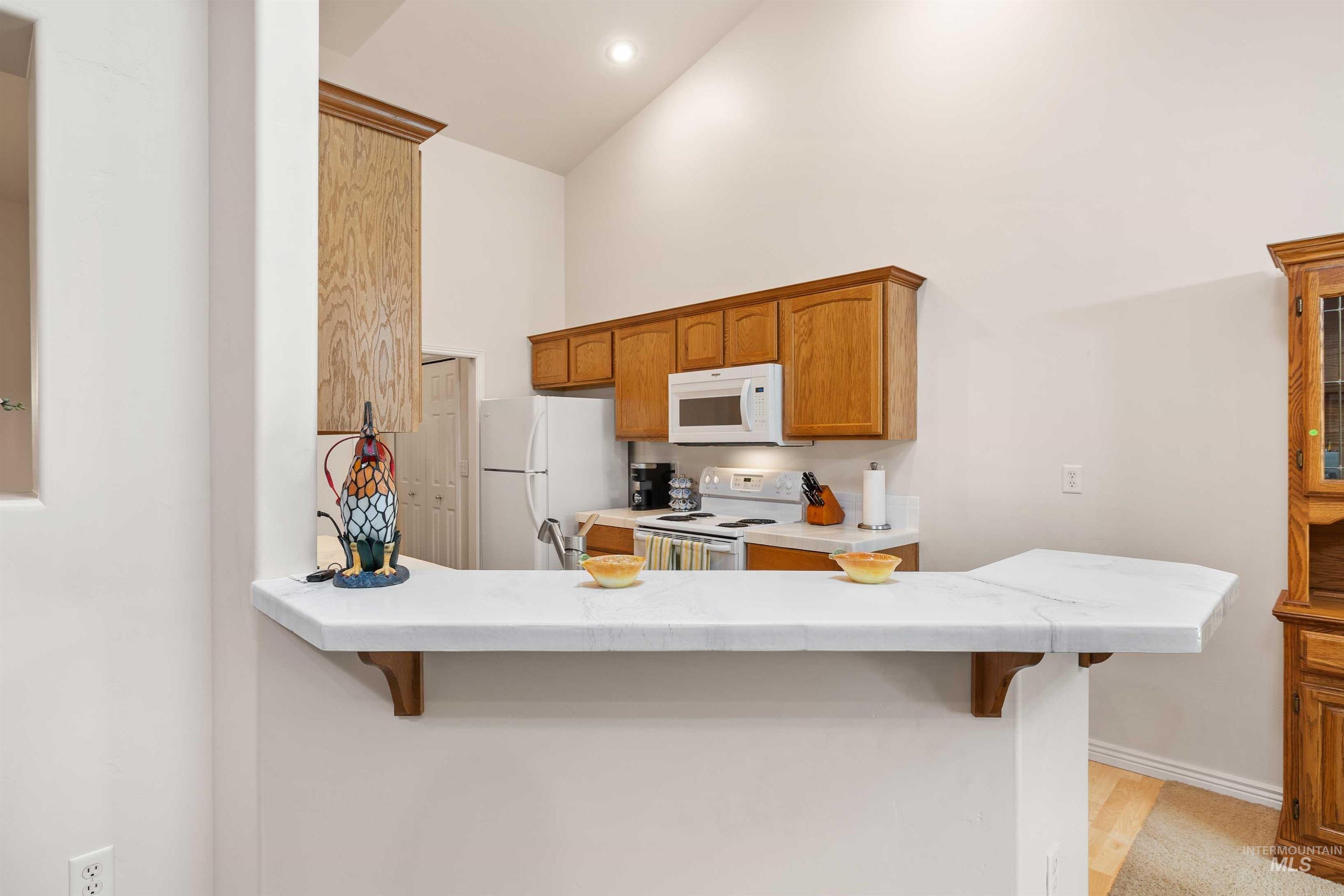 Kitchen with a breakfast bar area, white appliances, brown cabinetry, high vaulted ceiling, and a peninsula