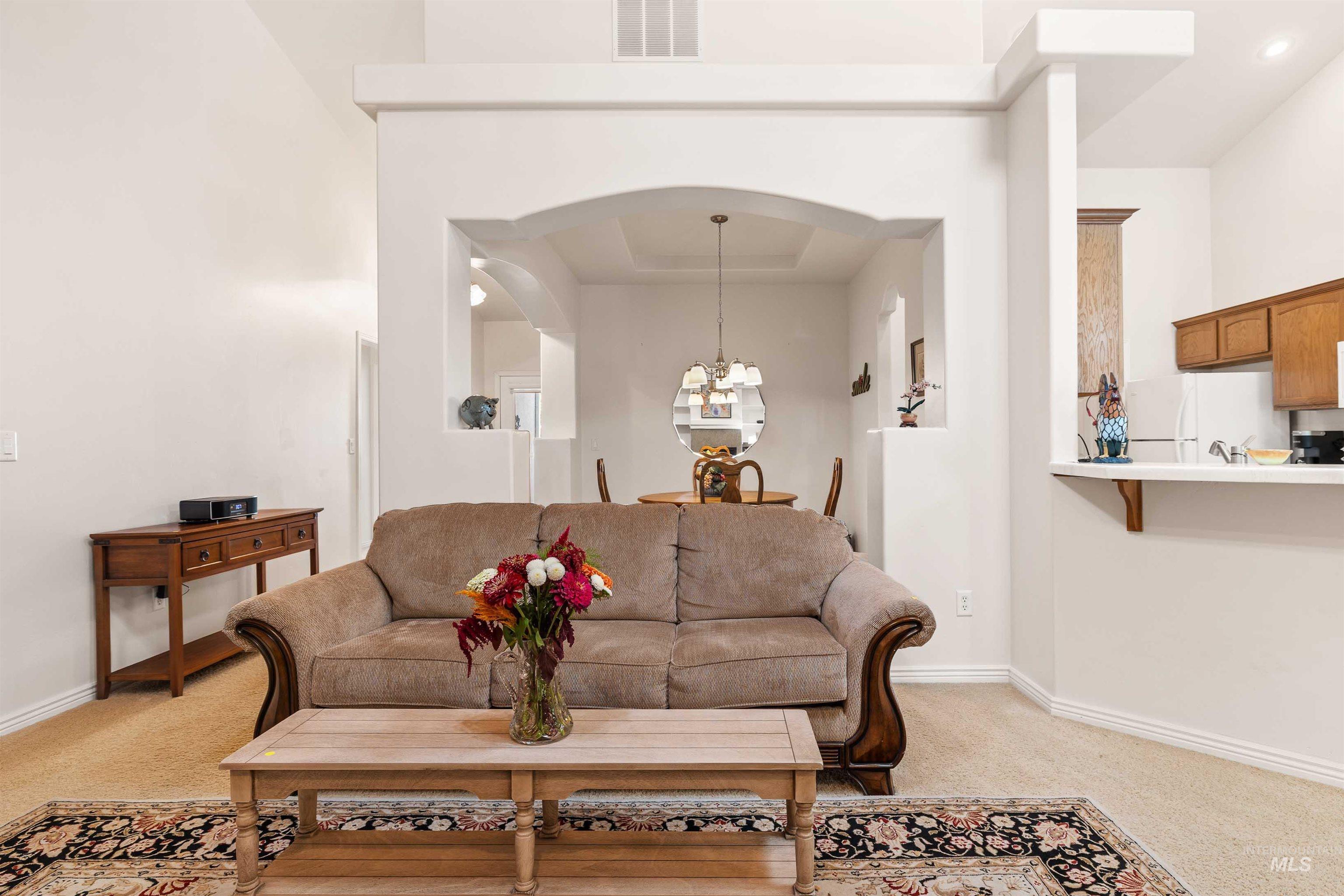 Living area with light colored carpet, a chandelier, and arched walkways