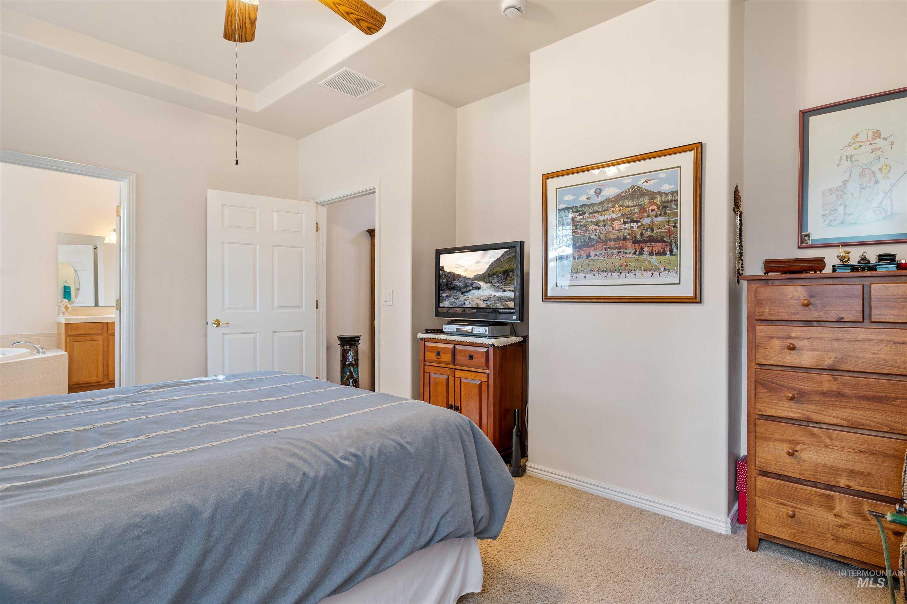 Bedroom with light colored carpet, a ceiling fan, and ensuite bathroom