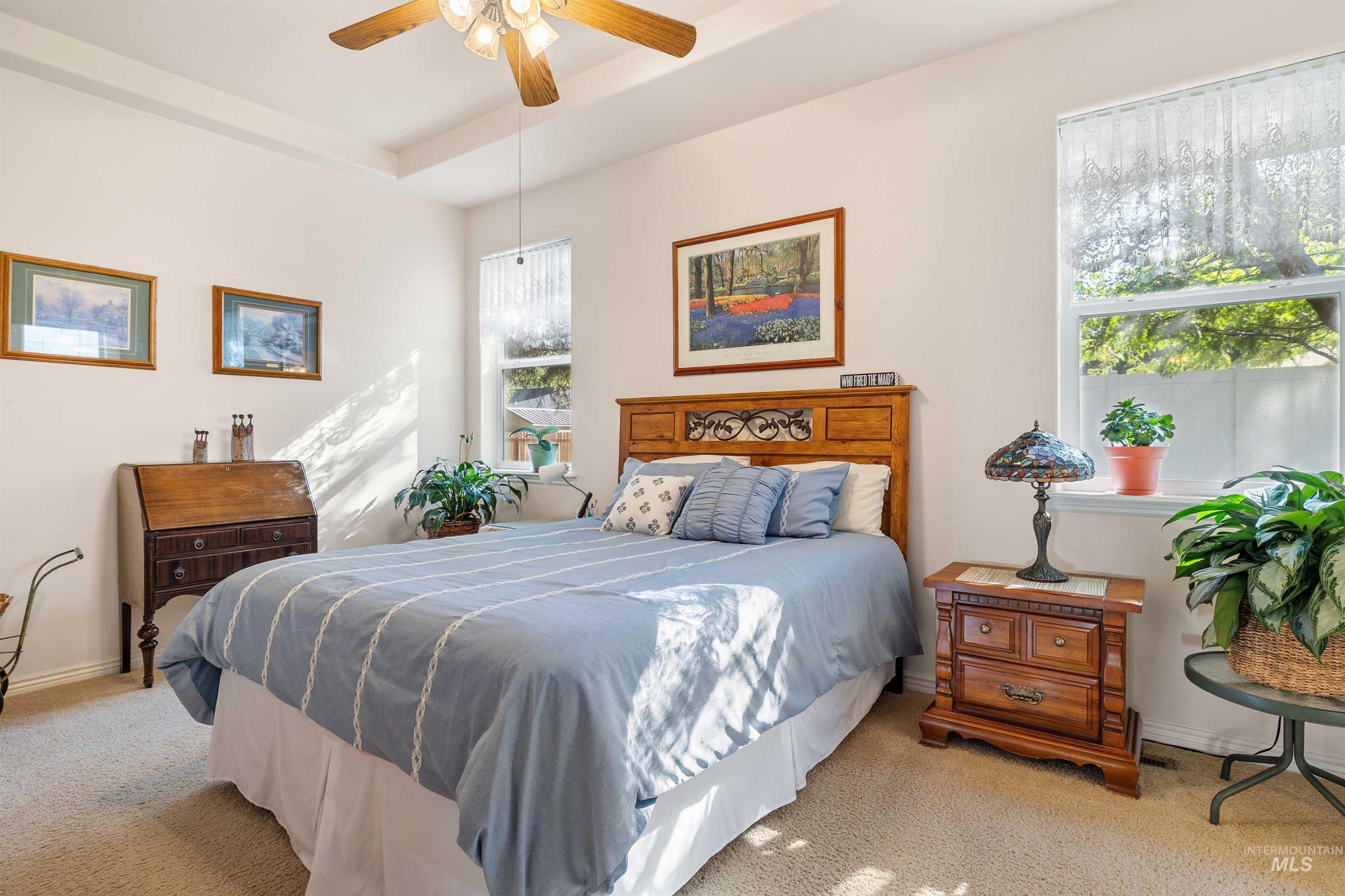 Carpeted bedroom with a raised ceiling and ceiling fan