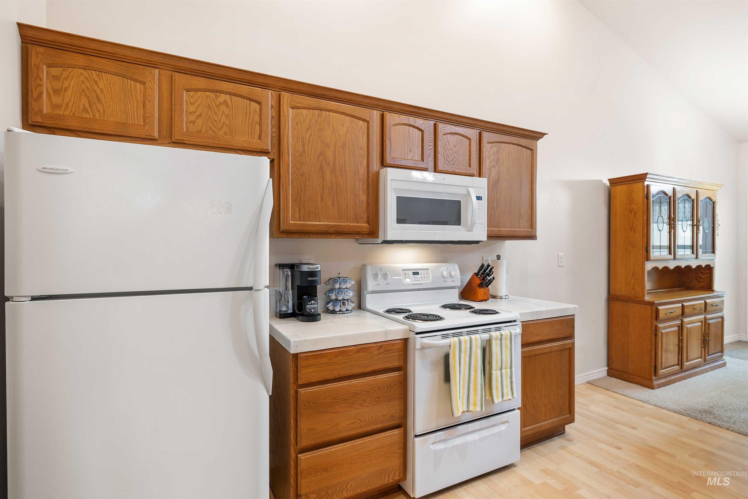 Kitchen featuring white appliances, light countertops, light wood-style floors, and brown cabinetry