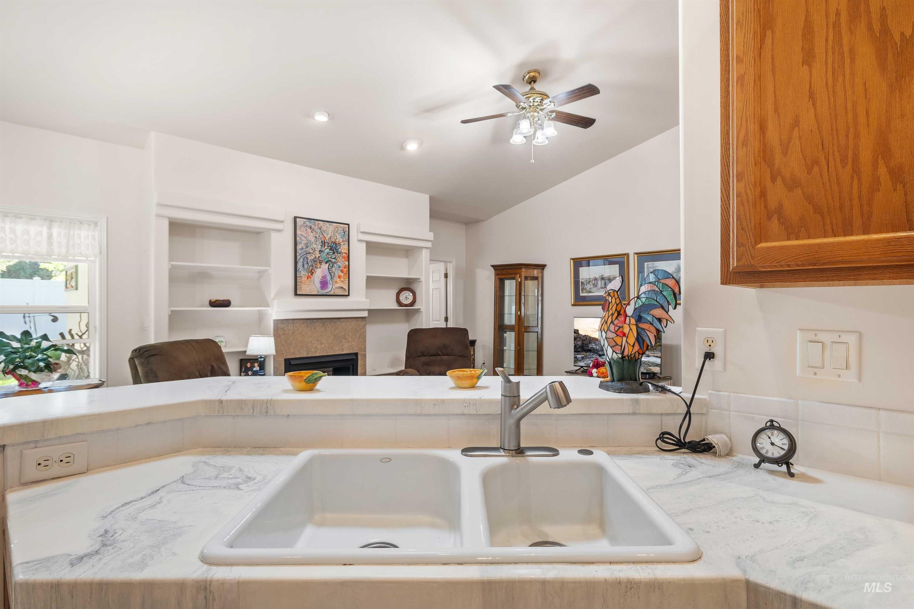 Kitchen featuring a fireplace, open floor plan, ceiling fan, lofted ceiling, and light stone countertops