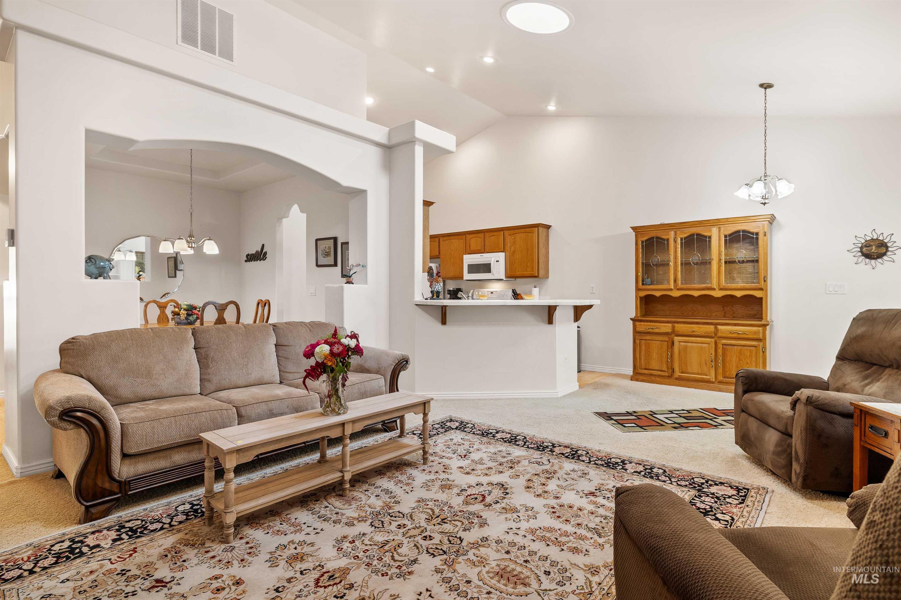 Living area featuring a chandelier, light colored carpet, high vaulted ceiling, arched walkways, and recessed lighting
