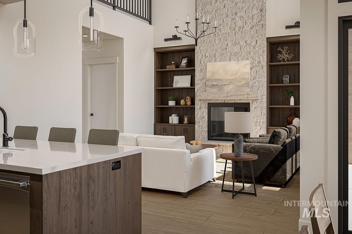 Living room featuring built in shelves, a high ceiling, a stone fireplace, and light wood-style floors