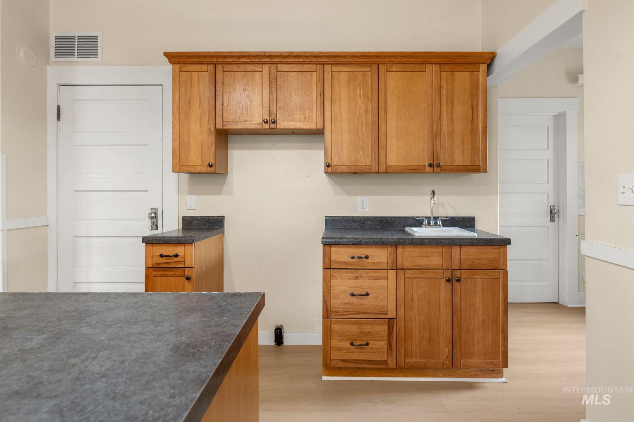 Kitchen with brown cabinets, dark countertops, and light wood-style flooring