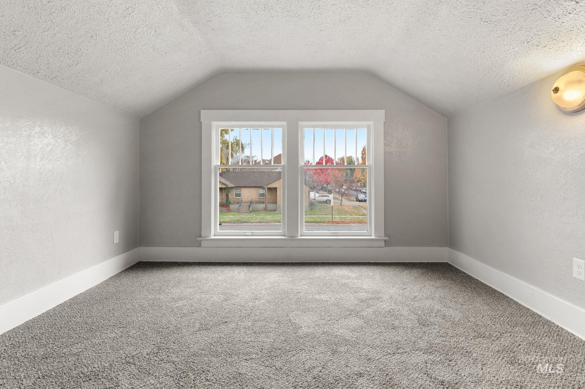 Additional living space featuring a textured wall, a textured ceiling, lofted ceiling, and carpet