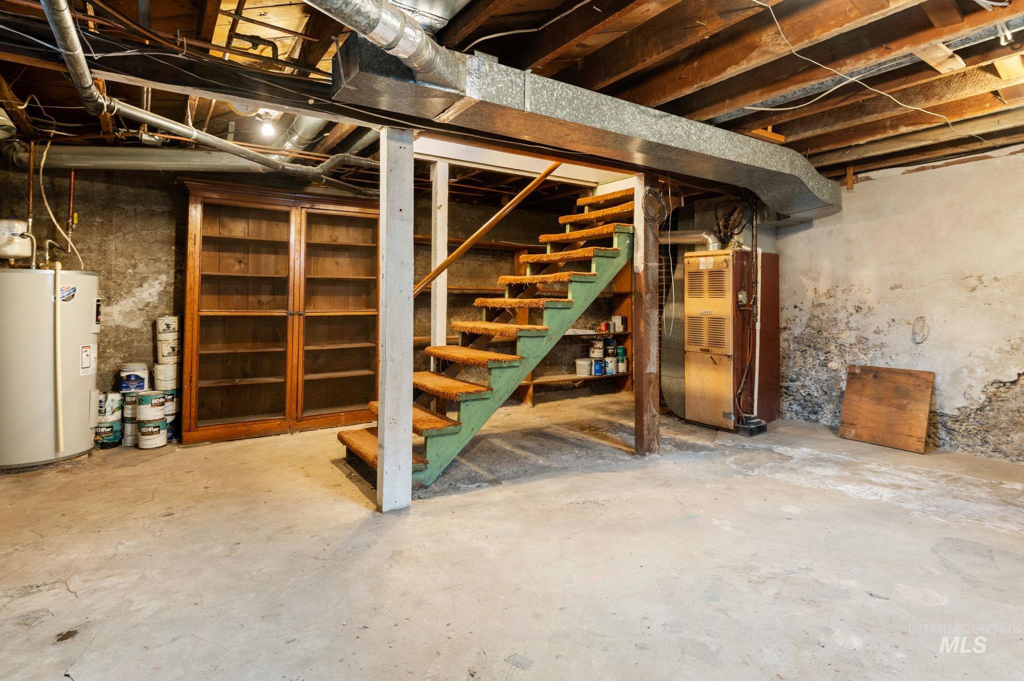 Unfinished below grade area with water heater, heating unit, and stairs