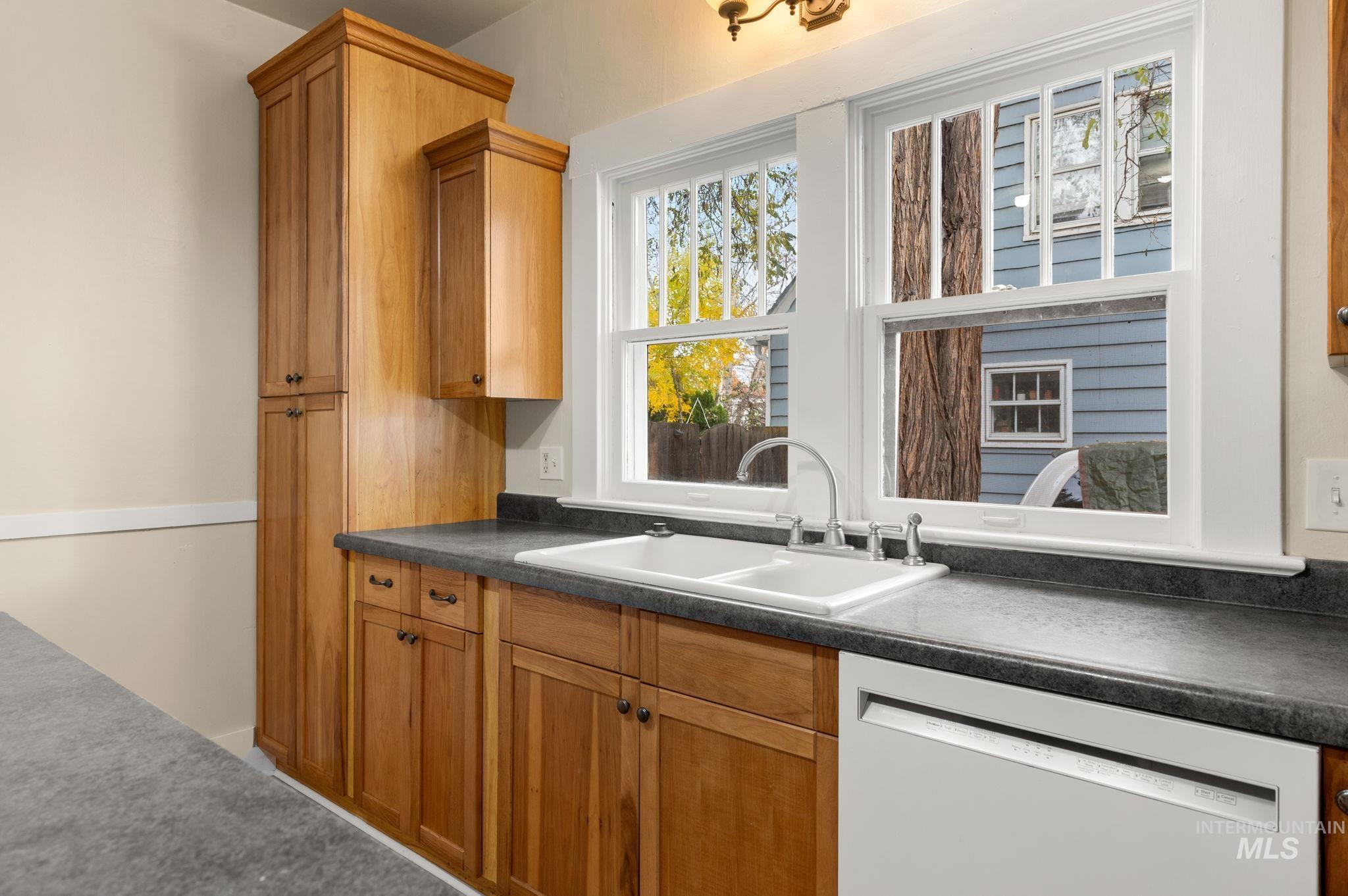 Kitchen with dark countertops, dishwasher, brown cabinetry, and carpet