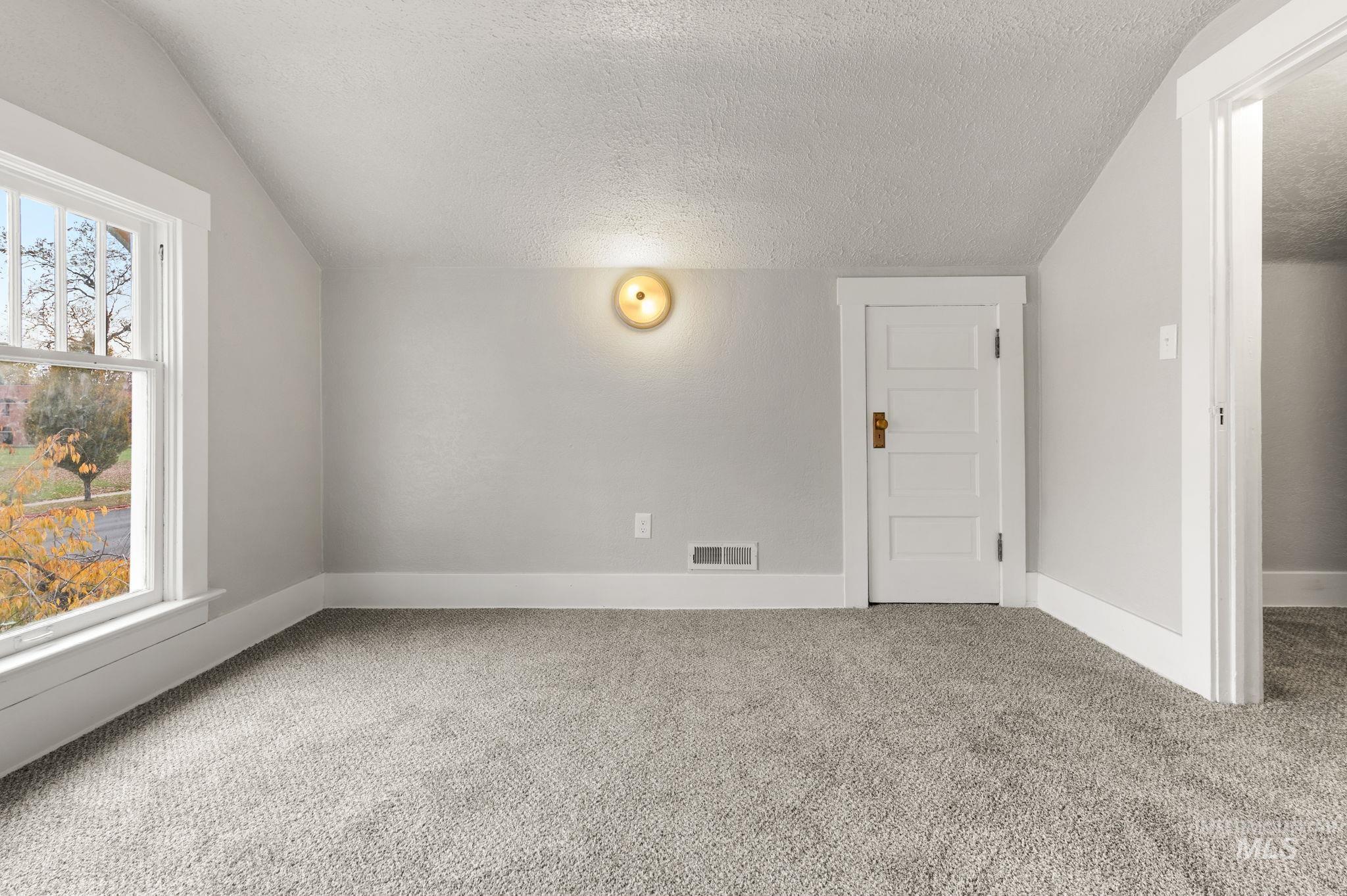Unfurnished room featuring a textured ceiling, light carpet, and vaulted ceiling