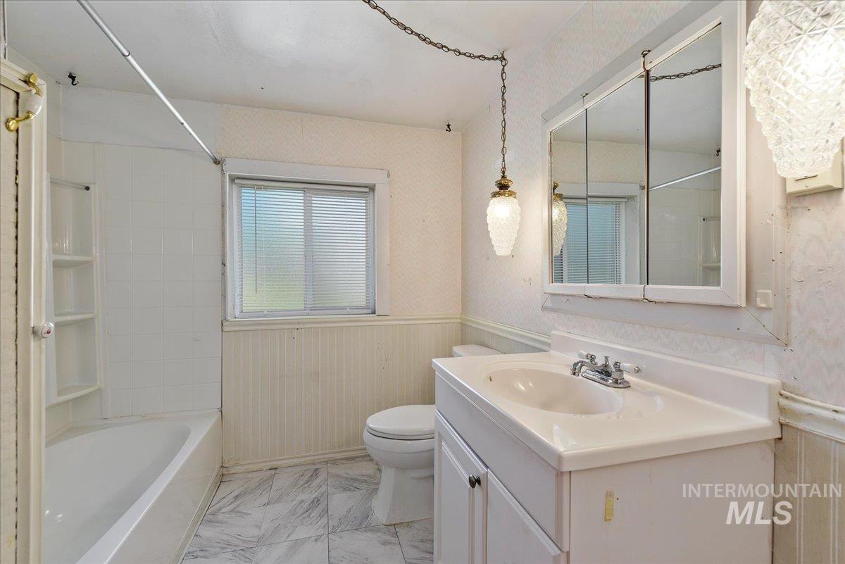 Bathroom featuring a white bathtub with integrated shelving, a white vanity with an integrated sink, a mirrored medicine cabinet, a window with blinds, and patterned tile flooring