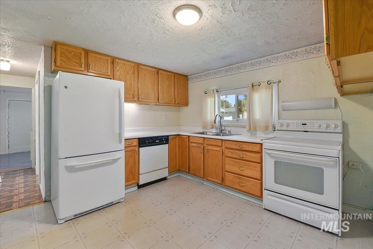 Kitchen featuring wood cabinetry, white countertops, a double basin sink with chrome faucet, and white appliances including a refrigerator, dishwasher, and electric range