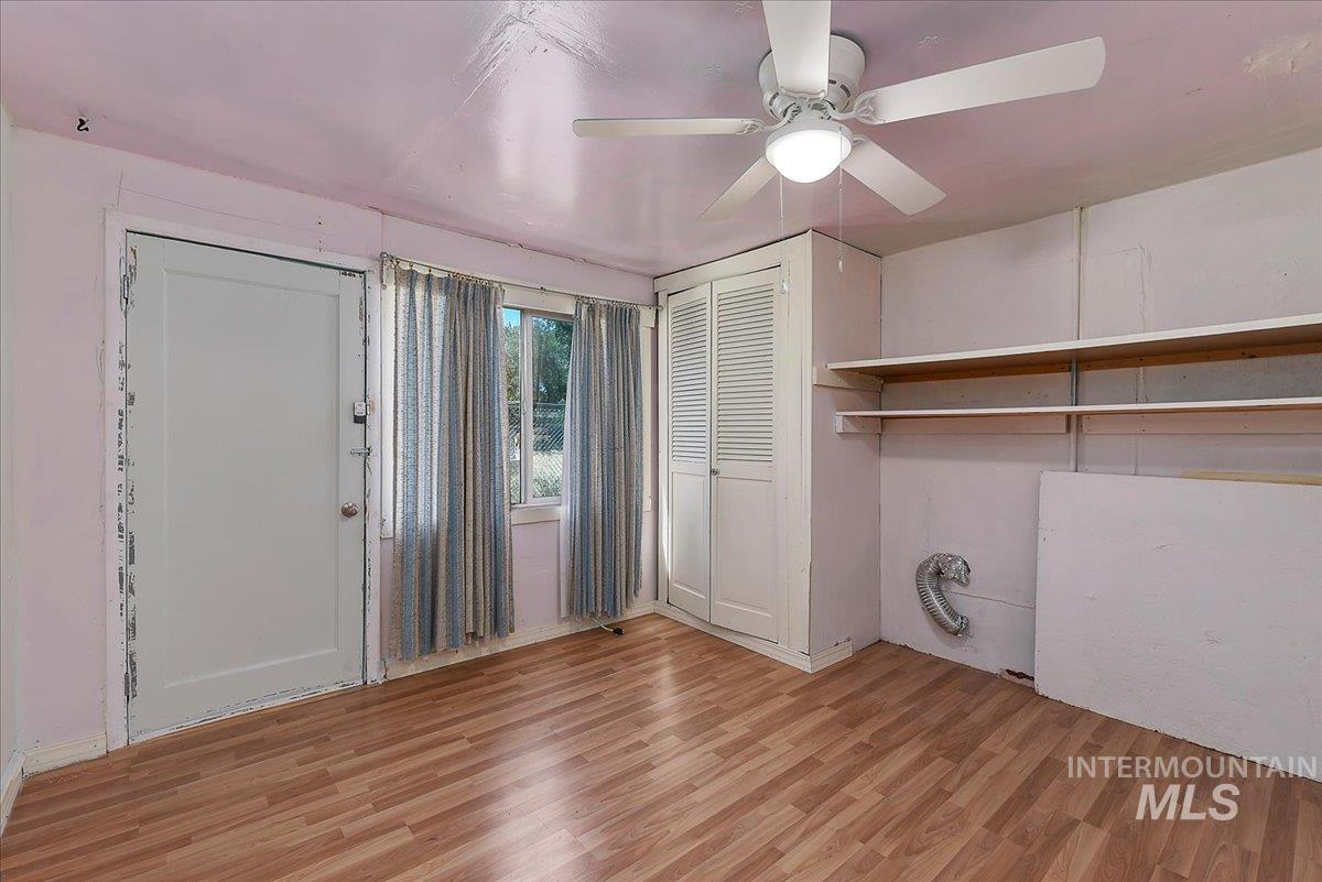 Room featuring wood-finish flooring, a ceiling fan with integrated lighting, two windows, and built-in closet storage with louvered doors