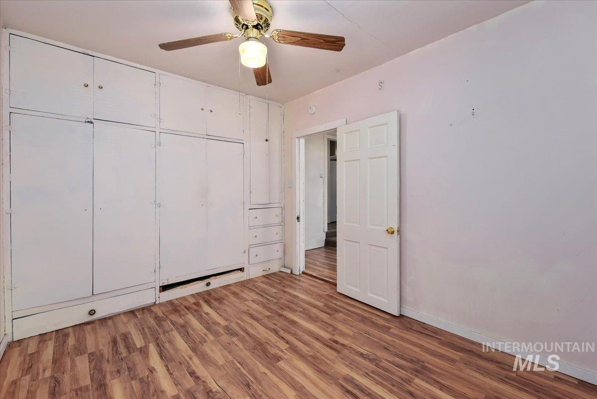 Room featuring wood-finish flooring, a ceiling fan with brass accents, and a built-in storage system with white paneled doors and drawers