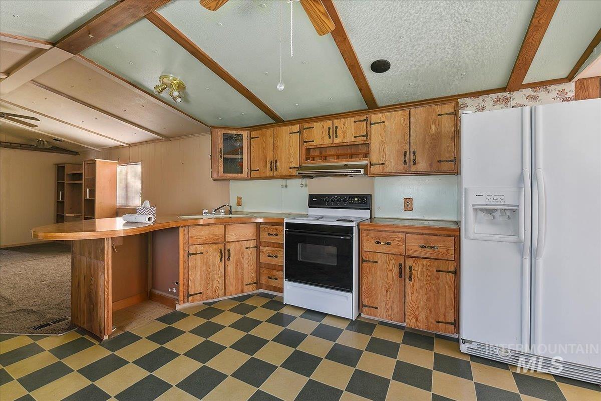 Kitchen featuring wood-finish cabinetry, a checkerboard-patterned floor, a built-in breakfast bar, a white refrigerator, and a white electric range