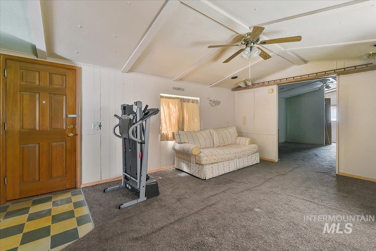 Vaulted ceiling with exposed beams and a ceiling fan, featuring a wood-panel entry door and checkered flooring at the entryway