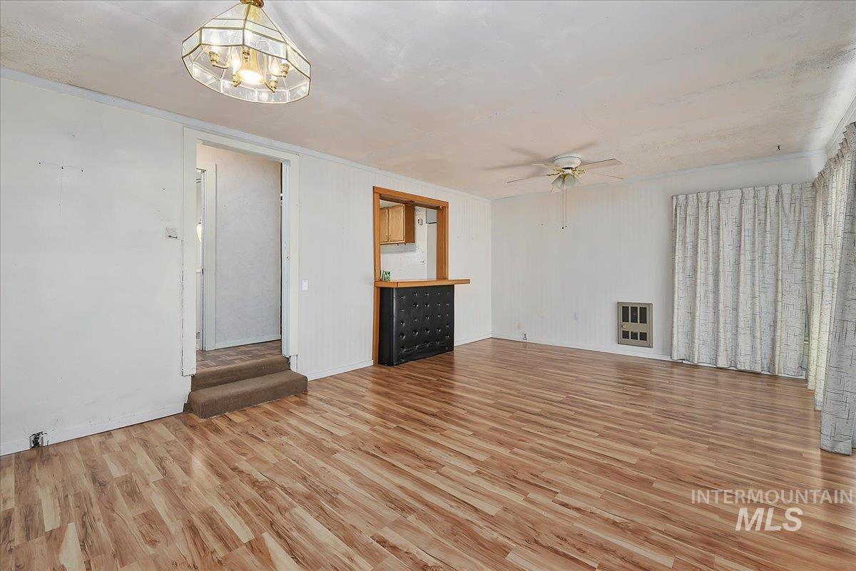 Open-concept room featuring wood-finish flooring, white wall panels, a built-in bar with wood cabinetry, a ceiling fan, and a large window with drapes