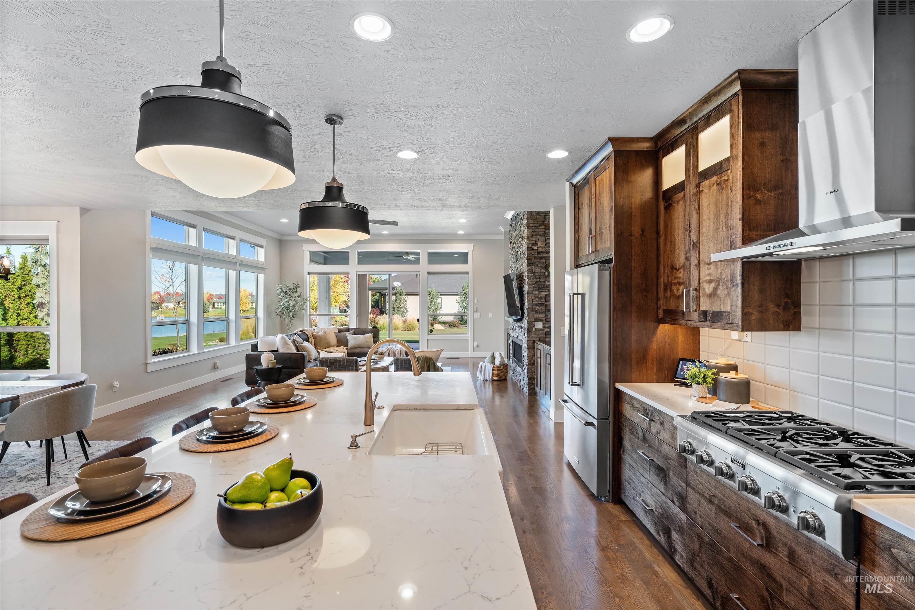 Two tone kitchen featuring stainless steel appliances, open floor plan, dark wood-style floors, a textured ceiling, and tasteful backsplash