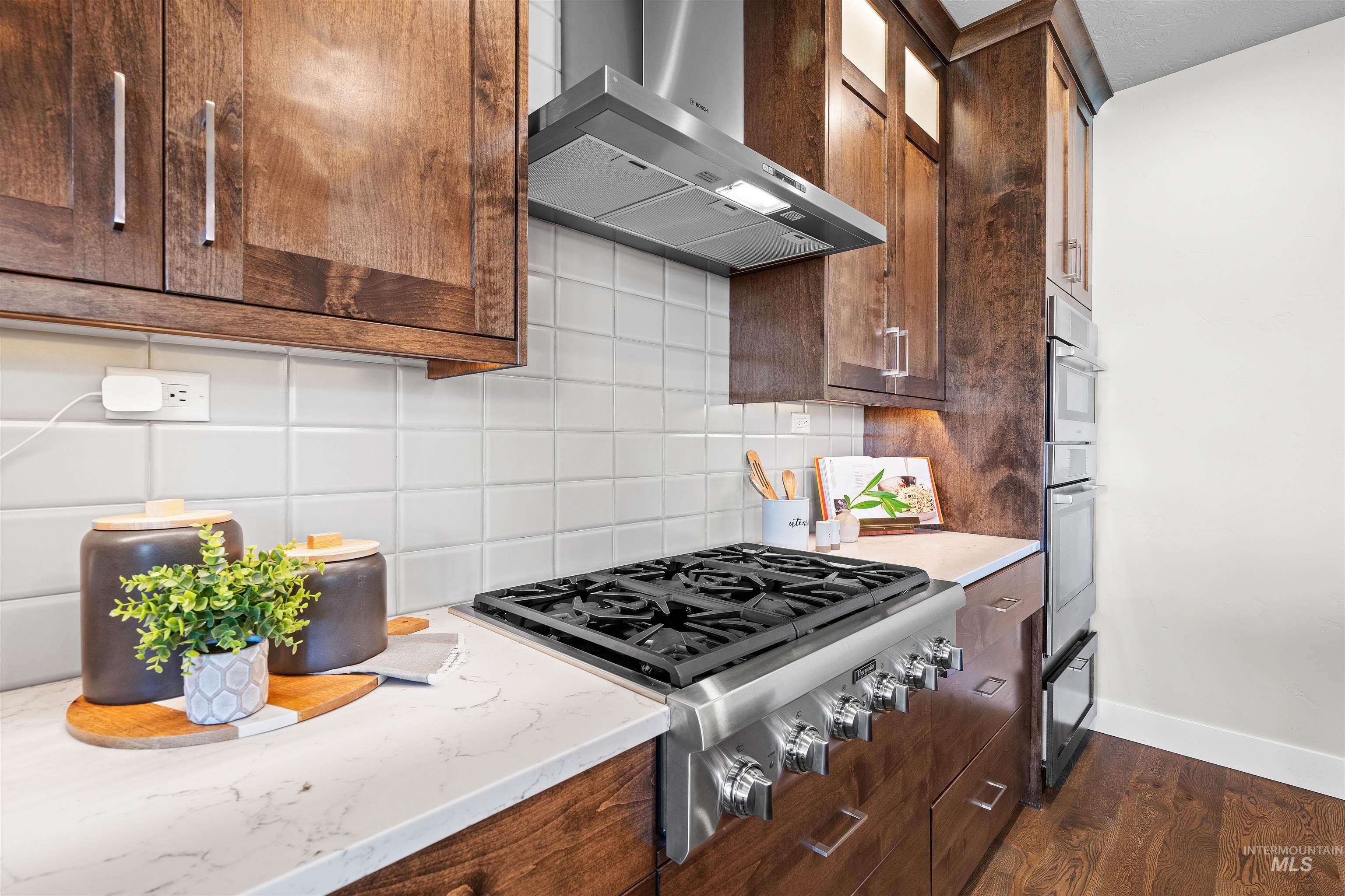 Kitchen with tasteful backsplash, stainless steel appliances, light stone counters, dark wood finished floors, and glass insert cabinets