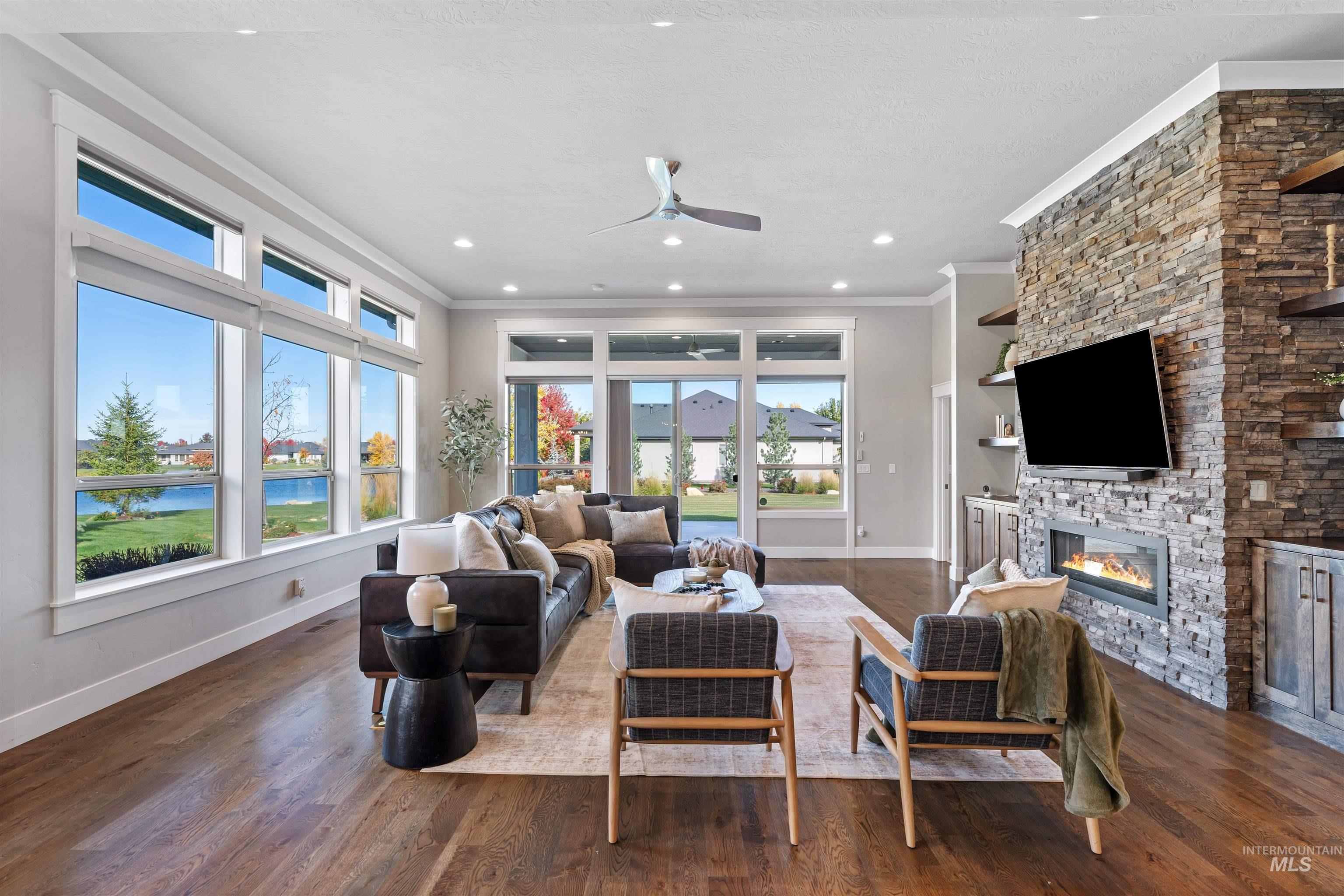 Living area with a fireplace, dark wood-style flooring, ceiling fan, crown molding, and a water view