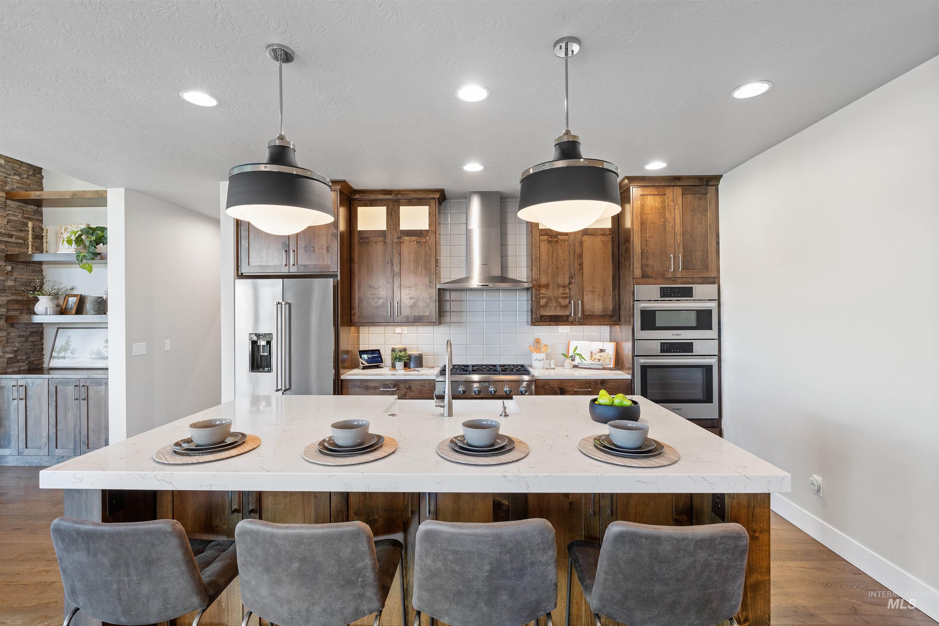 Kitchen featuring dark wood-type flooring, decorative light fixtures, a center island with sink, stainless steel appliances, and tasteful backsplash