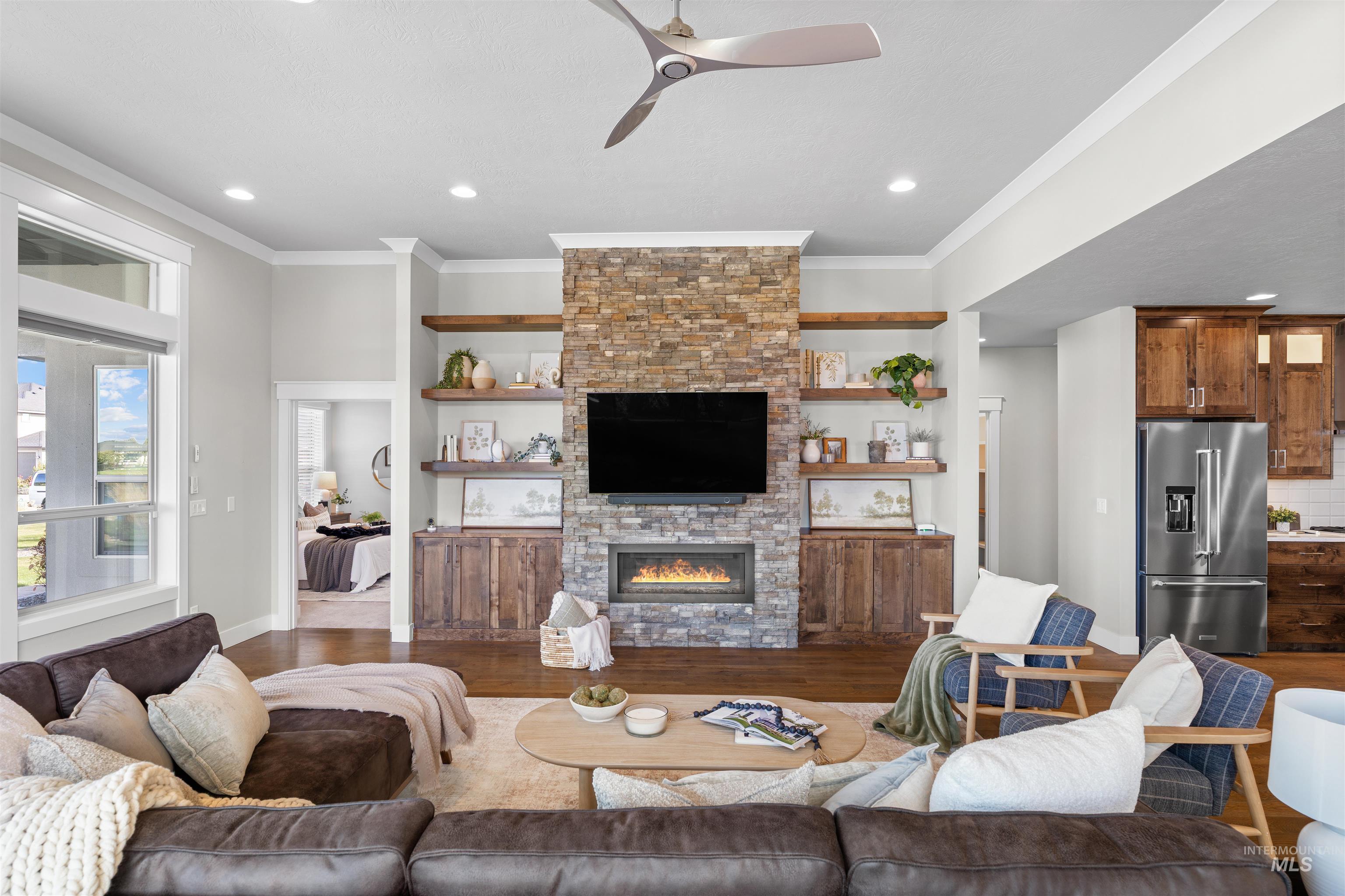 Living area featuring a ceiling fan, wood finished floors, a stone fireplace, ornamental molding, and recessed lighting