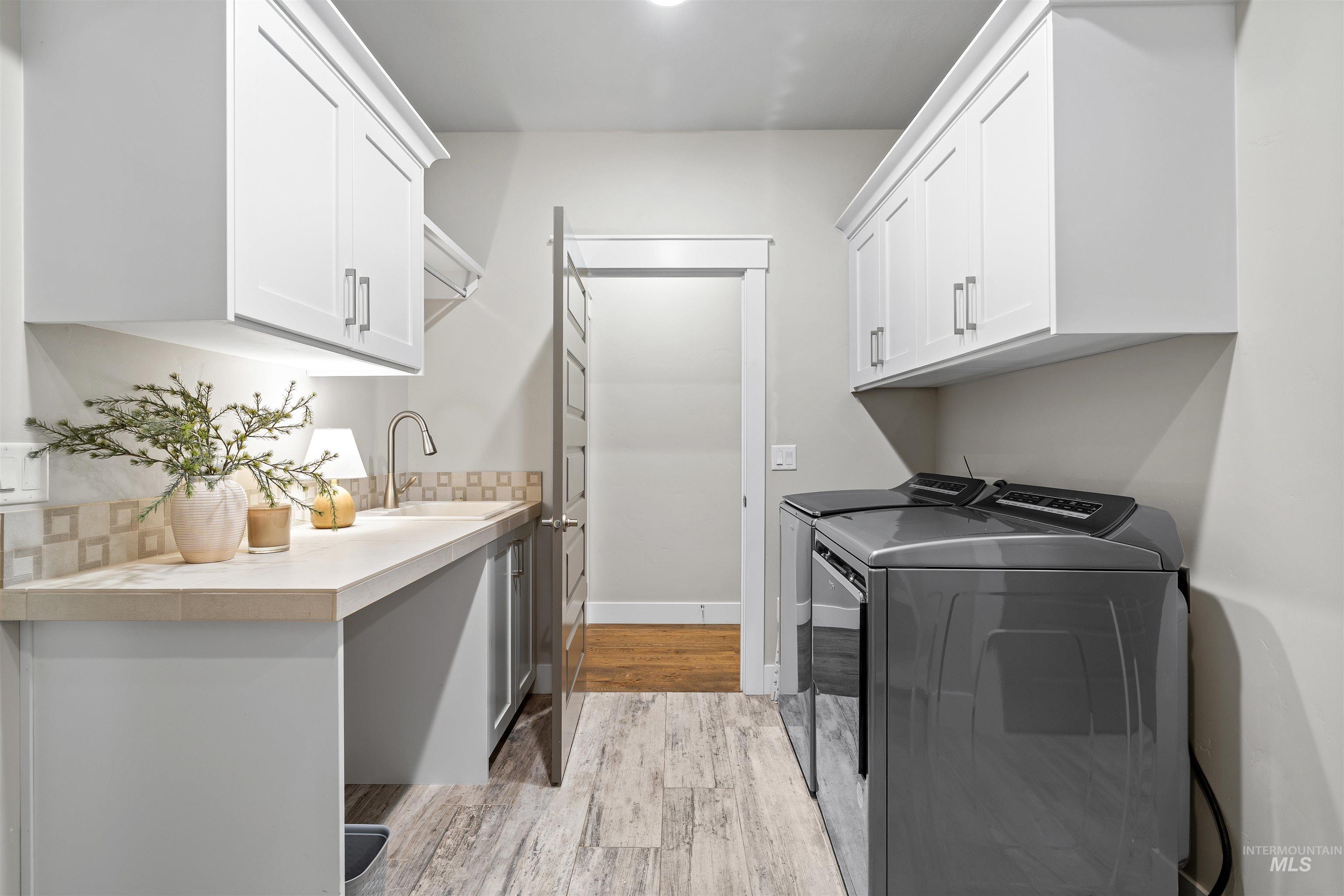 Laundry room with separate washer and dryer, light wood-style floors, and cabinet space