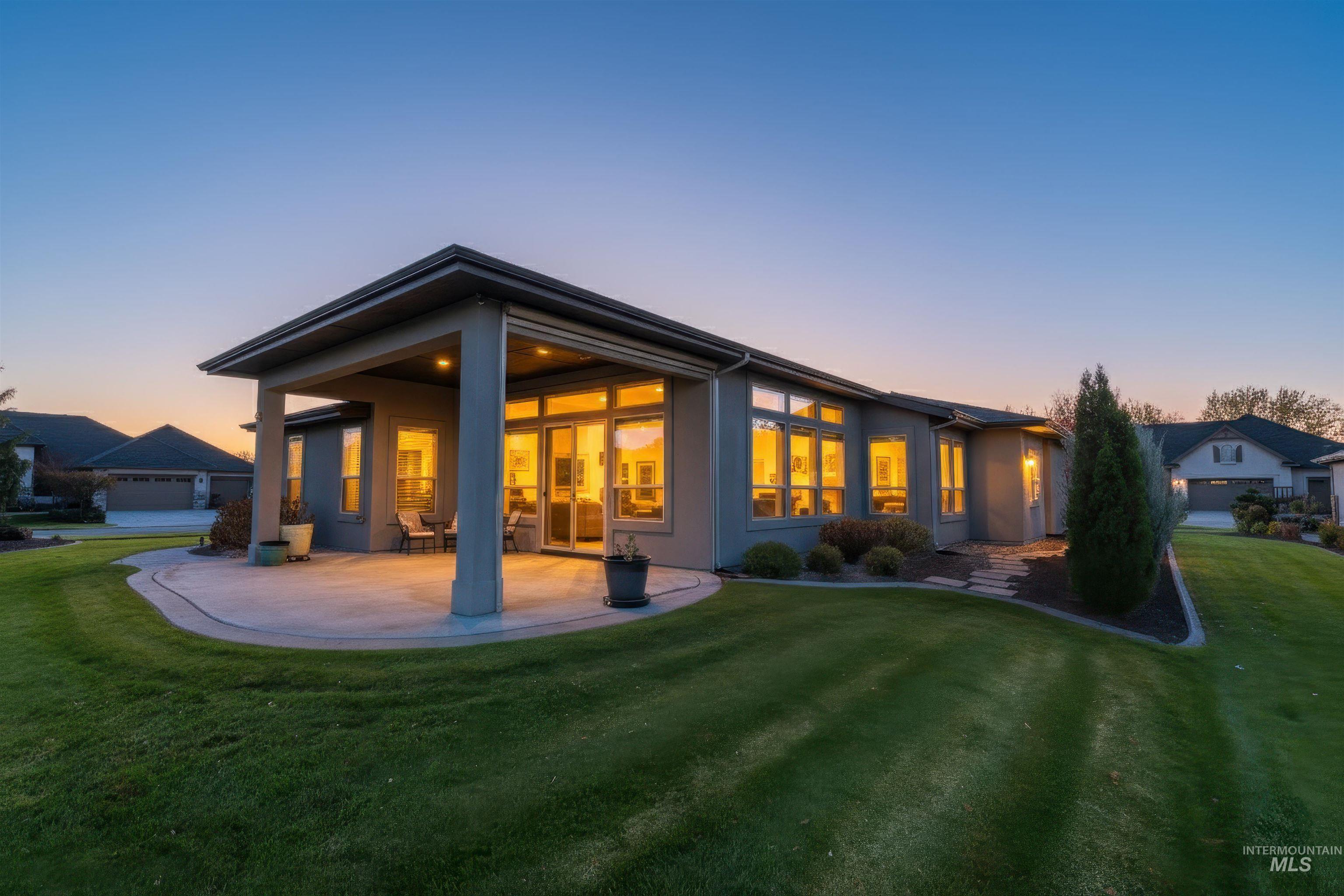 Back of property at dusk featuring a lawn, a patio, and stucco siding