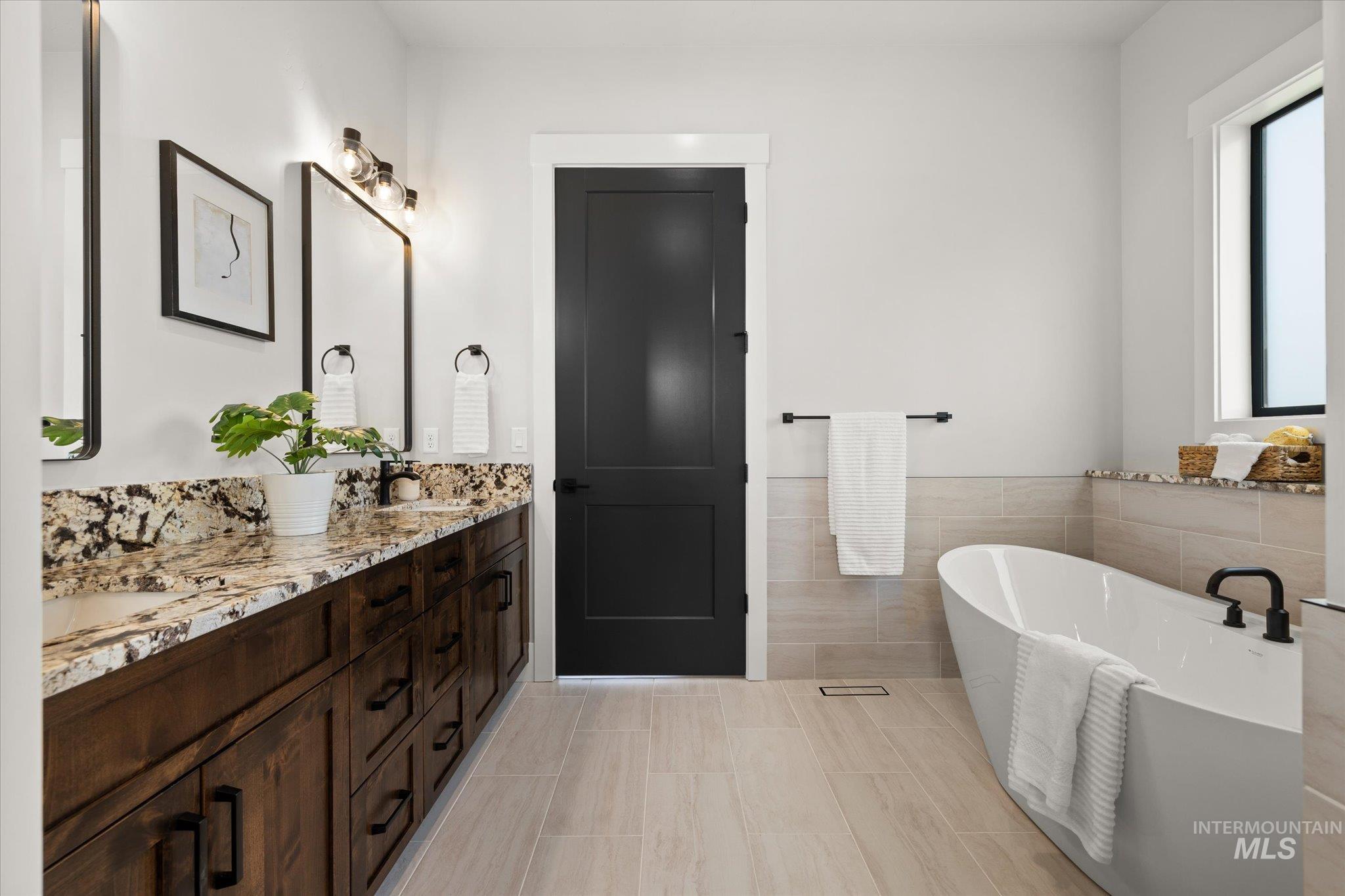 Bathroom with double vanity, a freestanding bath, tile walls, light tile patterned flooring, and a wainscoted wall