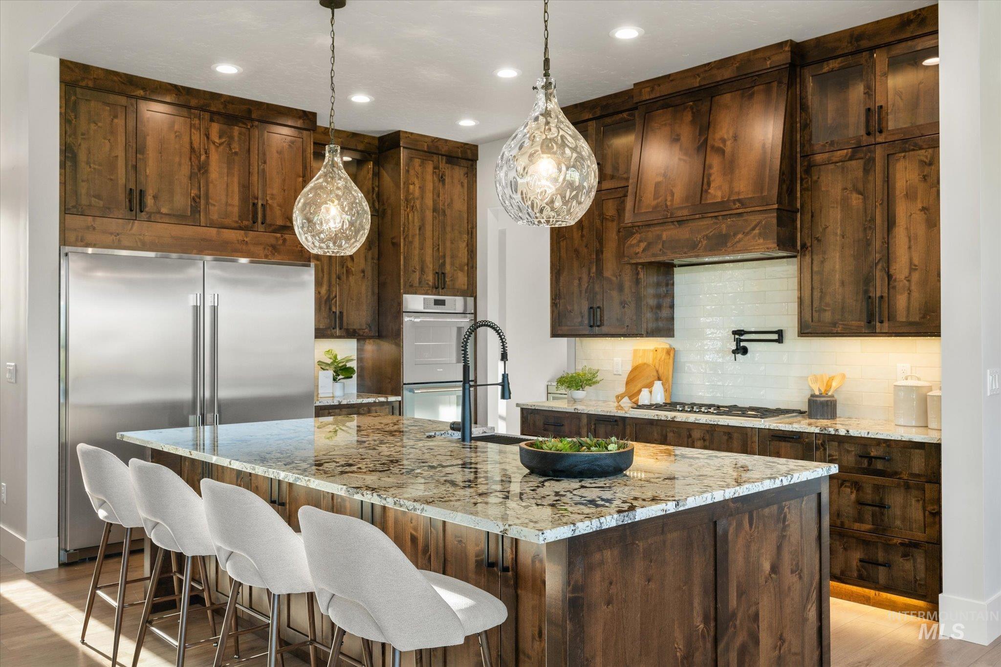 Kitchen with hanging light fixtures, appliances with stainless steel finishes, light stone countertops, tasteful backsplash, and light wood-style flooring