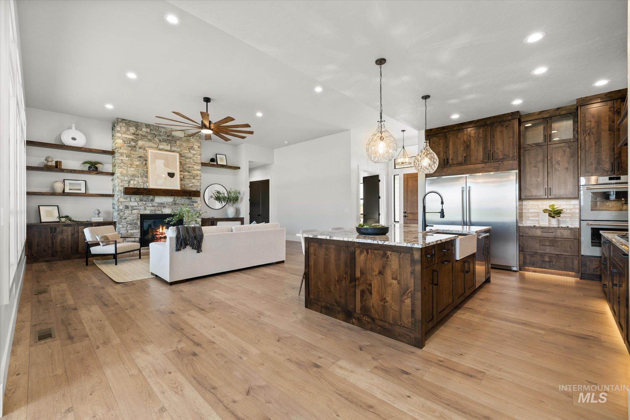 Kitchen with dark brown cabinets, light stone countertops, hanging light fixtures, open floor plan, and a stone fireplace