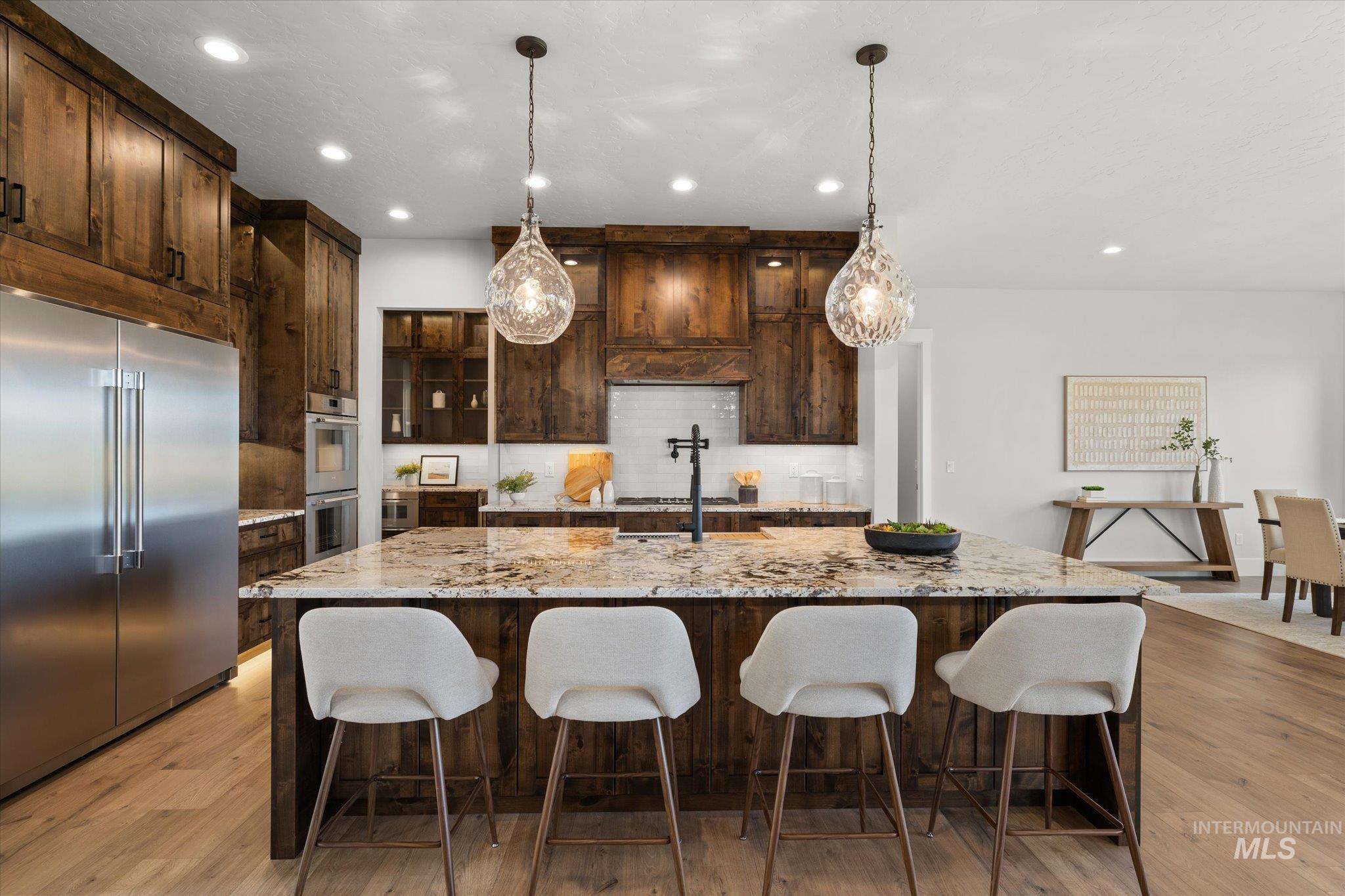 Kitchen featuring light stone counters, dark brown cabinetry, appliances with stainless steel finishes, hanging light fixtures, and recessed lighting