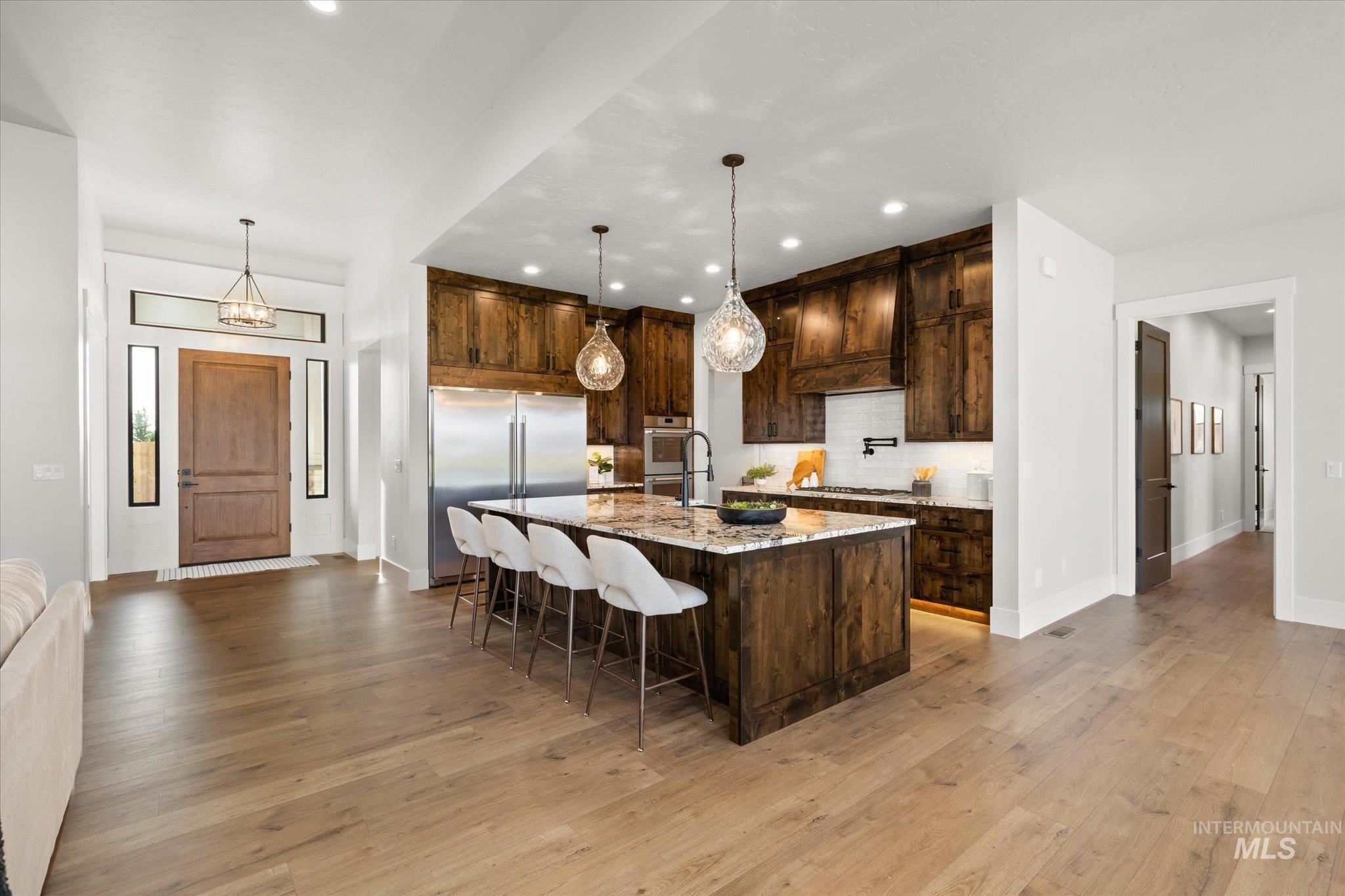 Kitchen with light stone countertops, a kitchen breakfast bar, pendant lighting, backsplash, and a large island with sink