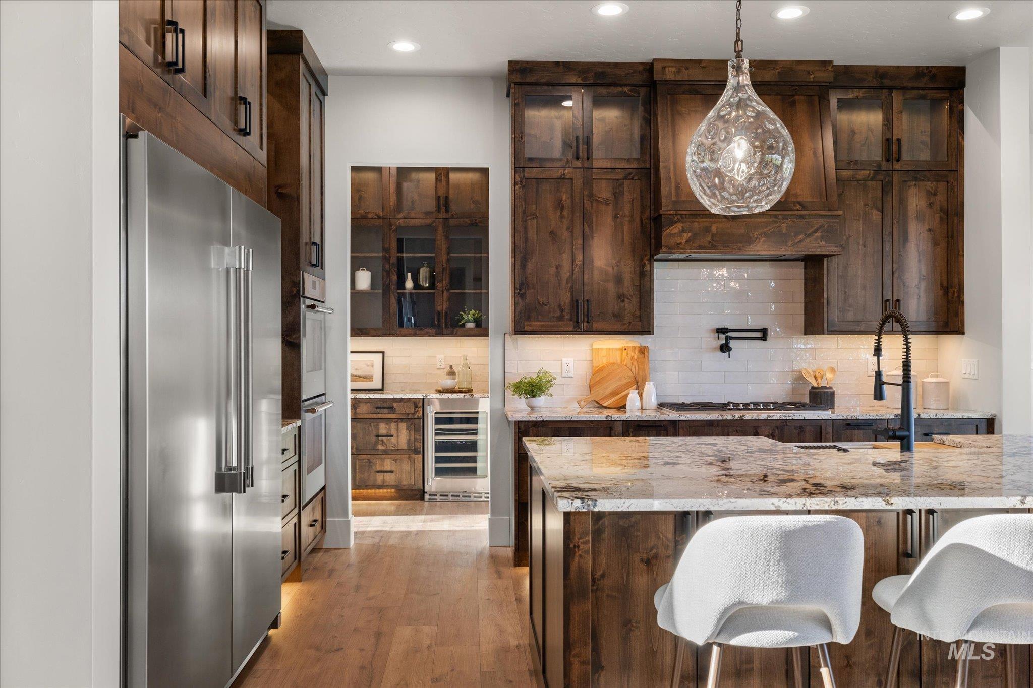 Kitchen with dark brown cabinetry, stainless steel appliances, hanging light fixtures, light stone countertops, and recessed lighting