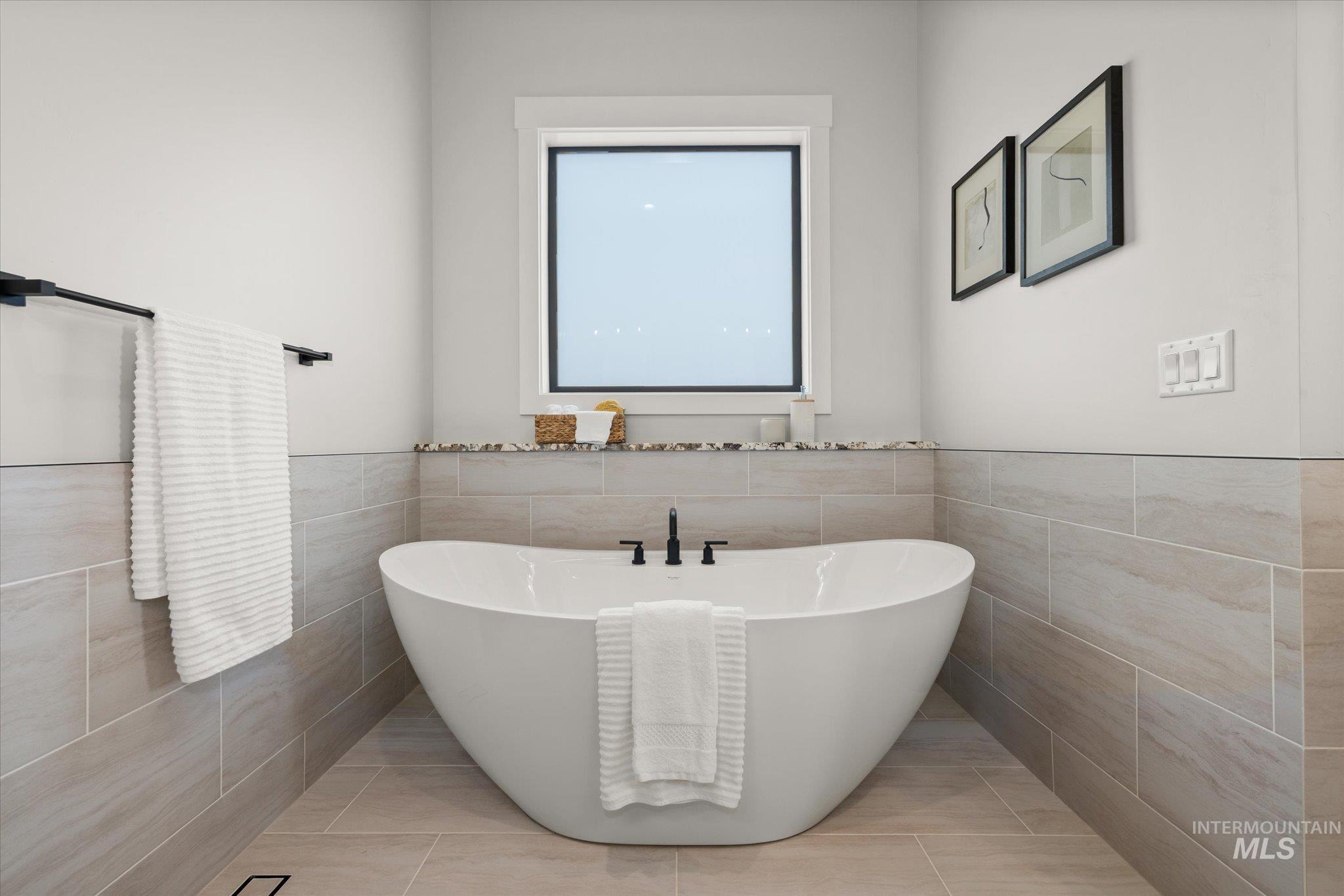 Bathroom featuring tile walls, a soaking tub, light tile patterned floors, and wainscoting